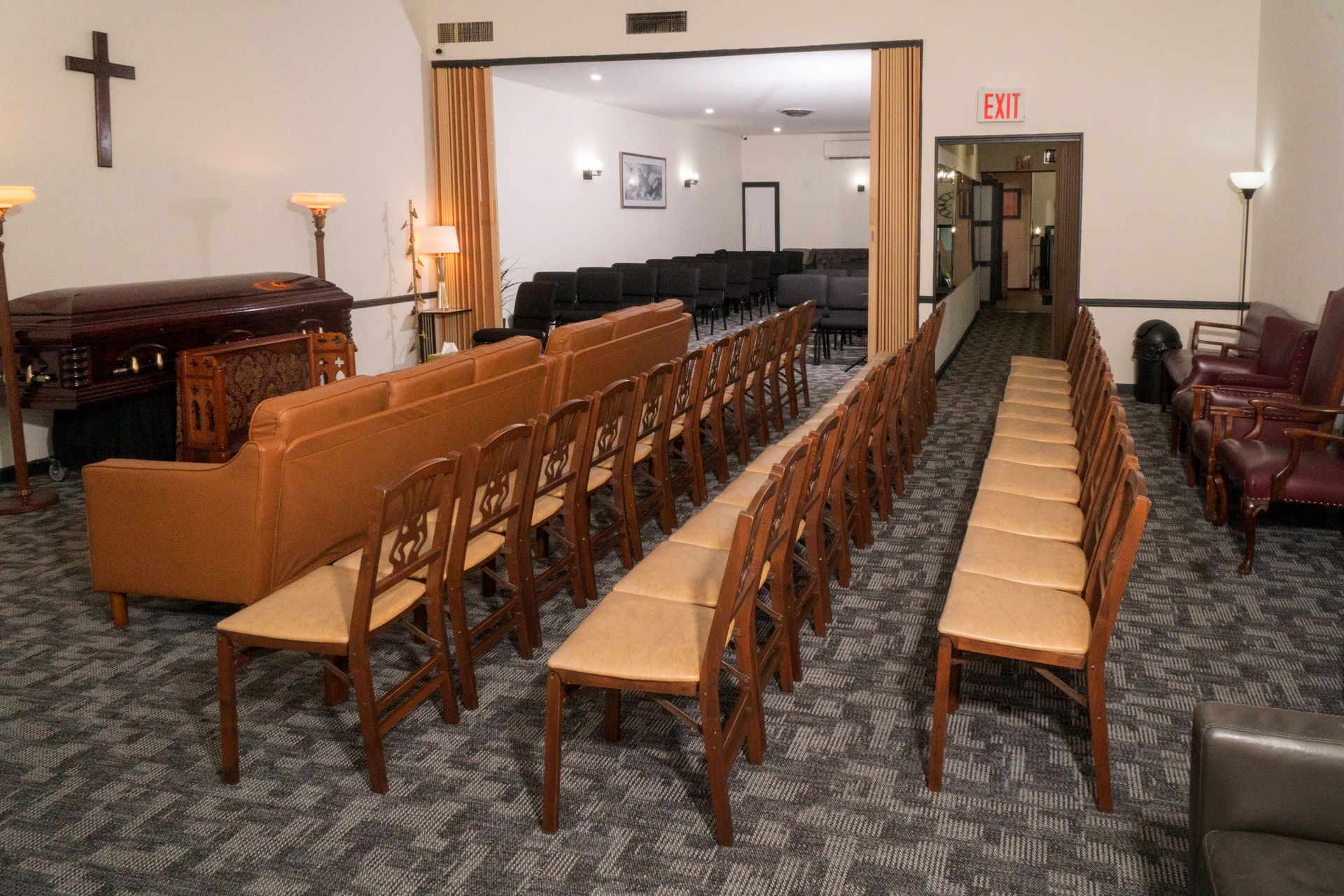 Empty church fellowship hall with rows of wooden chairs, leather sofas, and a podium near the front.