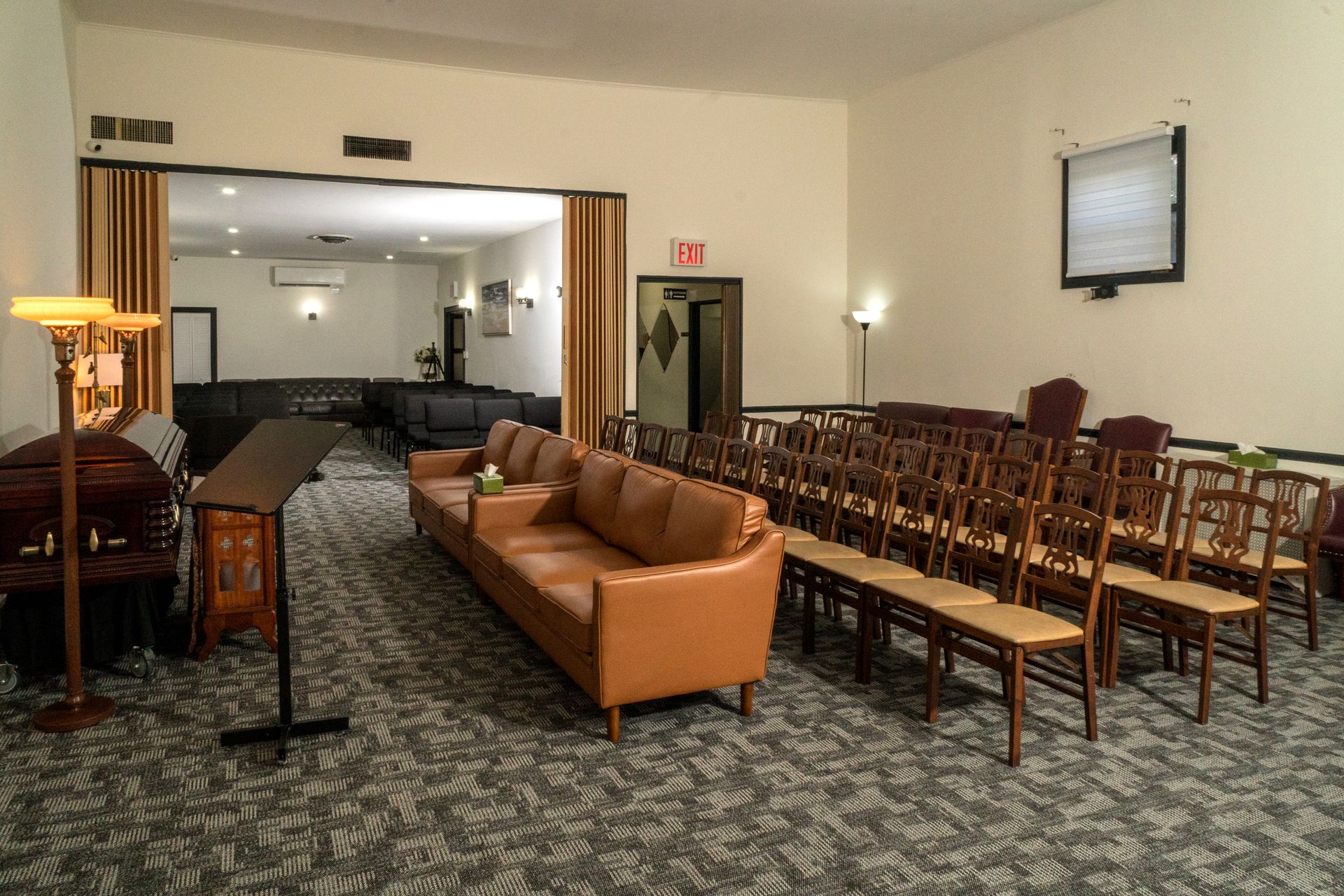 Empty banquet room with rows of chairs facing a front area, lit by warm lamps and curtains.