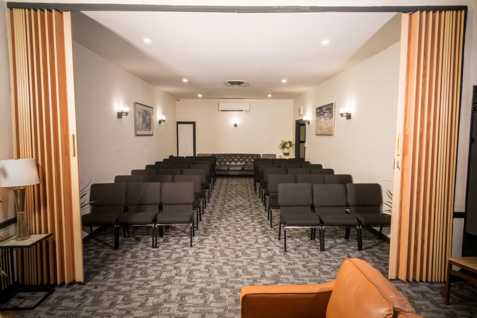 Small conference room with rows of black chairs, beige curtains, and a projection screen at the front.