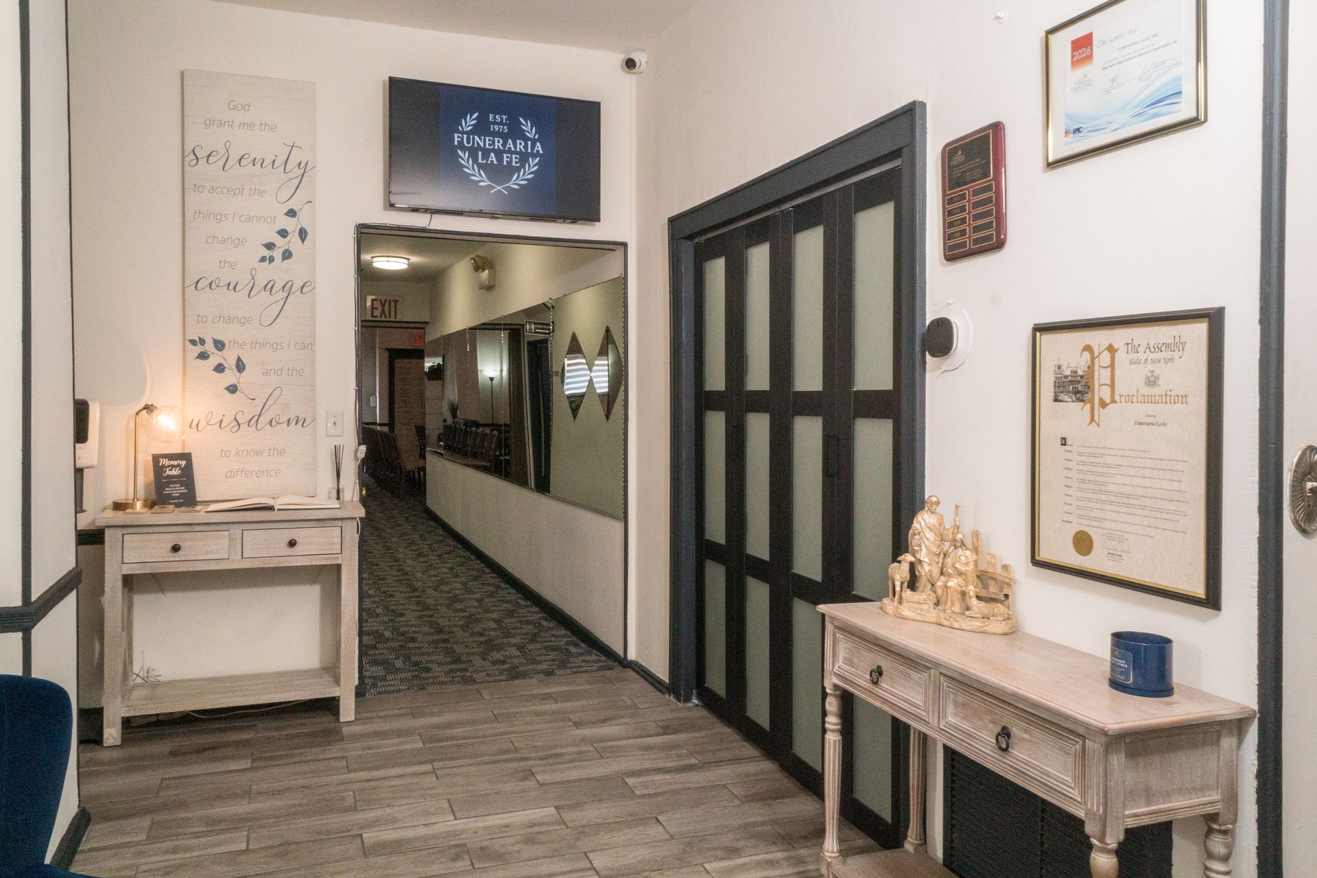 Bright hallway with framed art, marble tables, and black glass double doors in a stylish office lobby