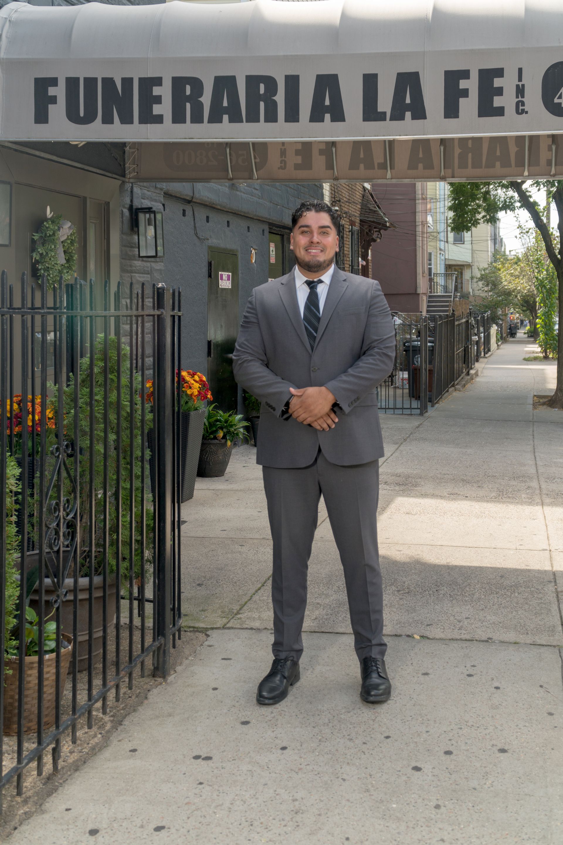 Man in a gray suit stands outside a funeral home entrance with a sign overhead.