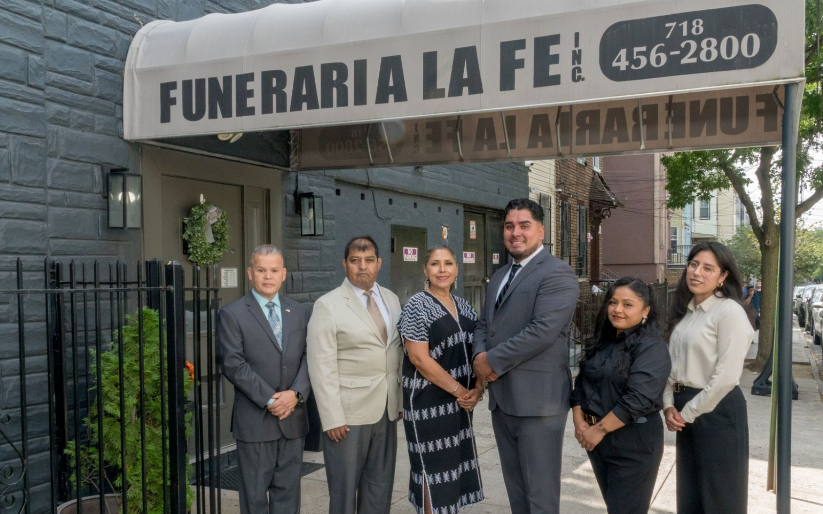 Six people stand outside Funeraria La Fe under a striped awning.