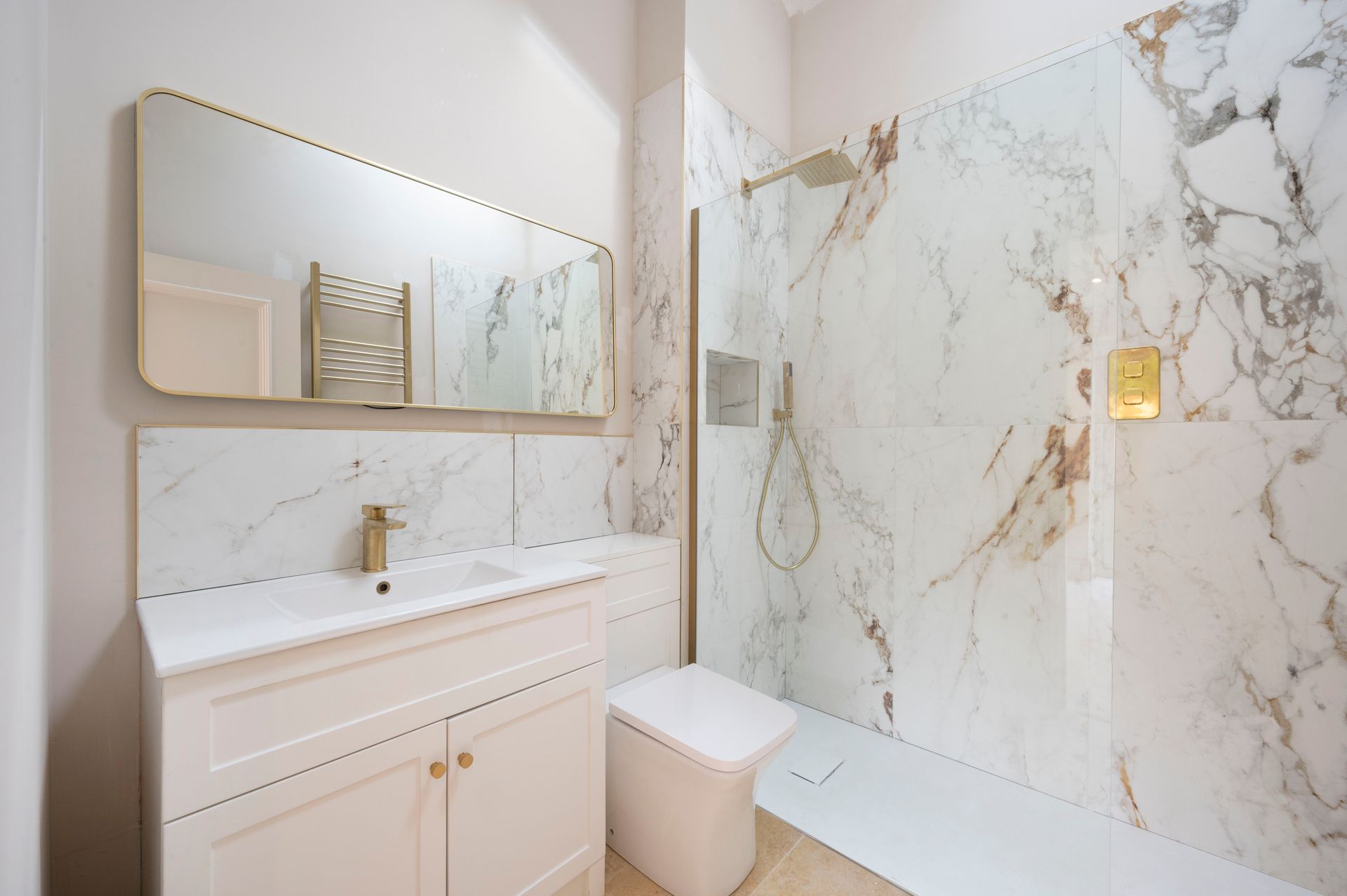 Modern bathroom with marble shower and vanity, gold fixtures, and a large mirror.
