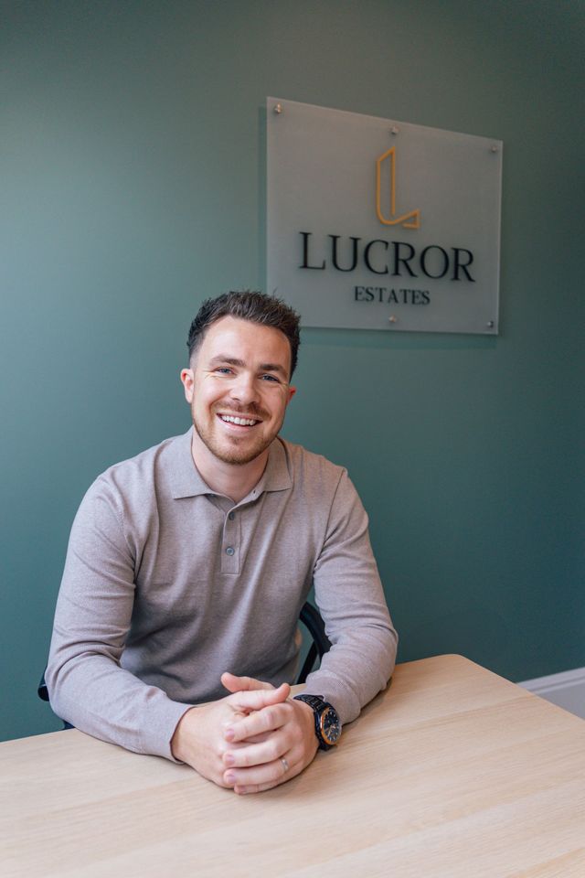 A man is sitting at a table in front of a sign that says lucror estates.