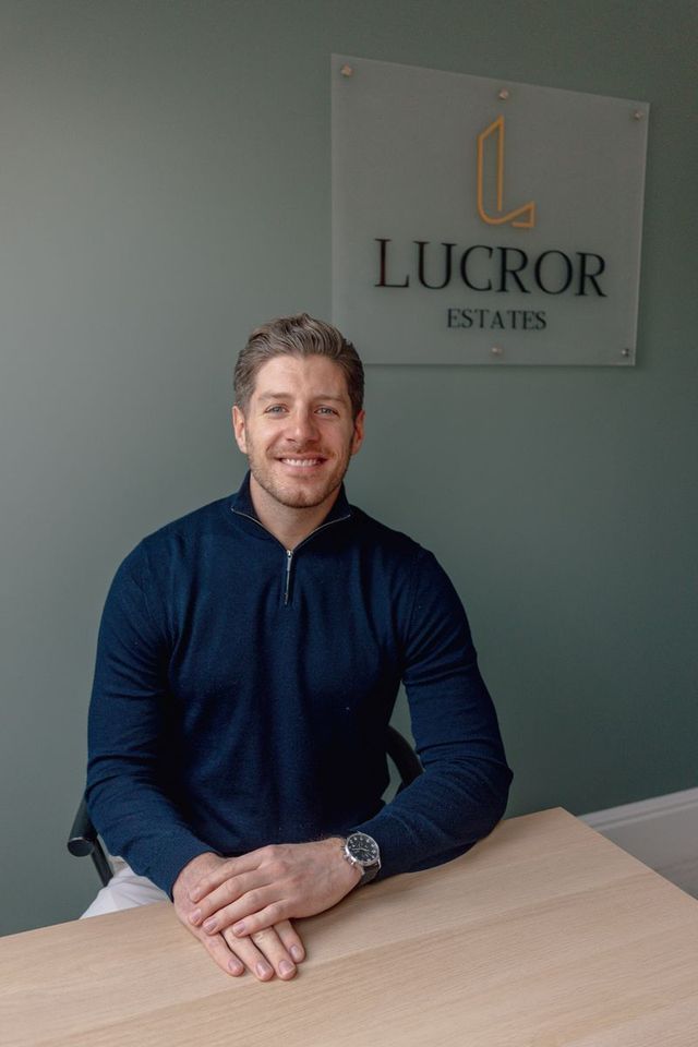 A man is sitting at a table in front of a sign that says lucror estates.
