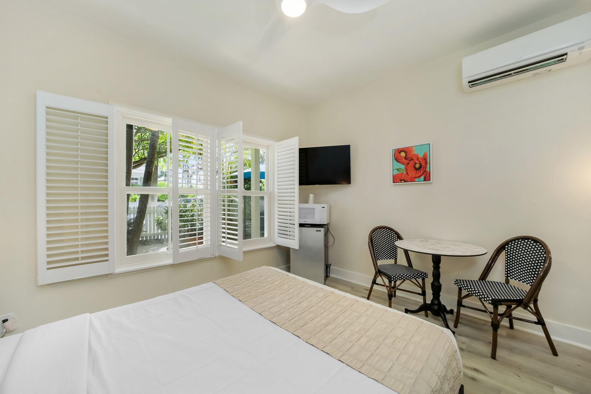 Bedroom with bed, shutters, small table, two chairs, and a TV.