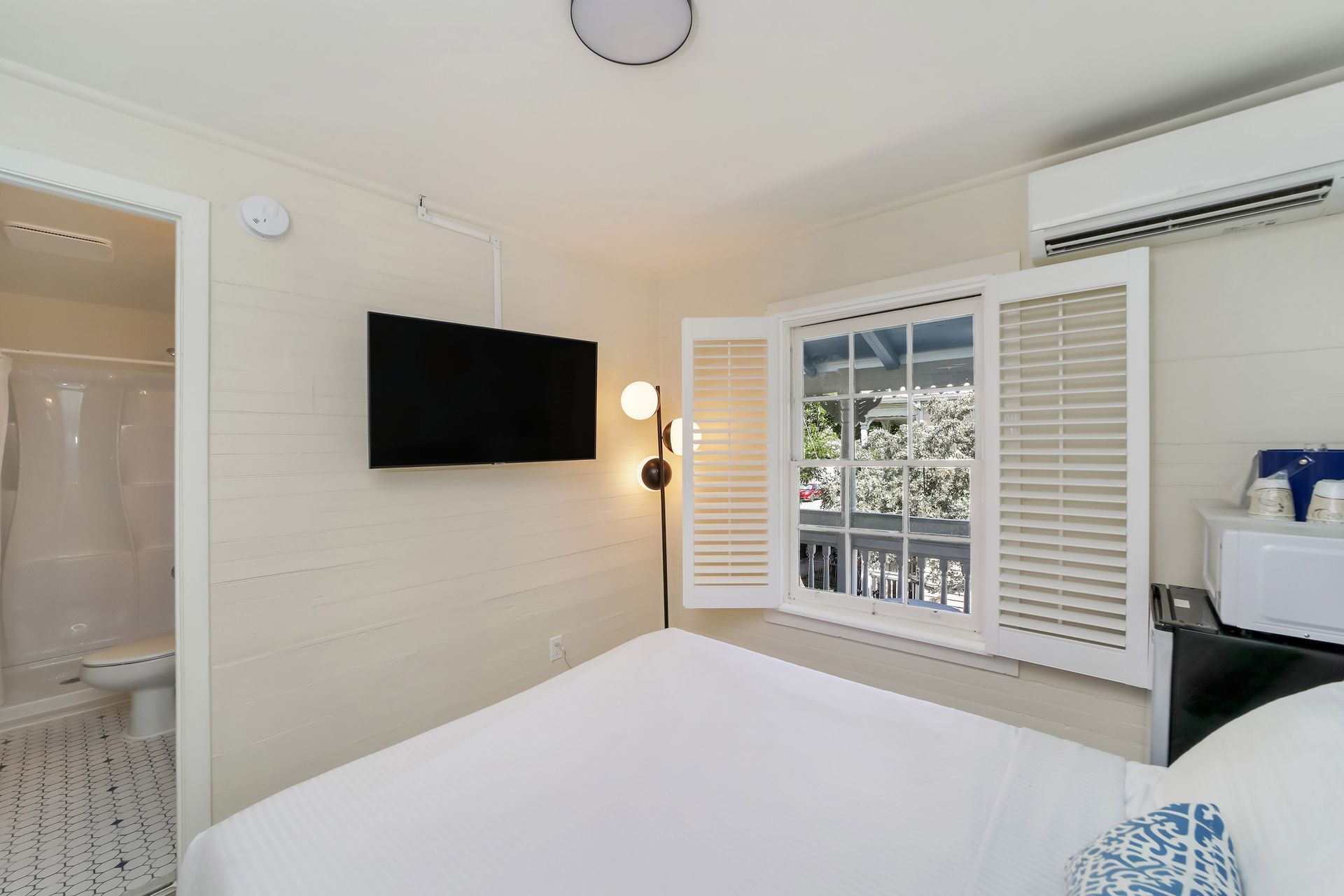 Bedroom with a bed, TV, window with shutters, and a small bathroom.