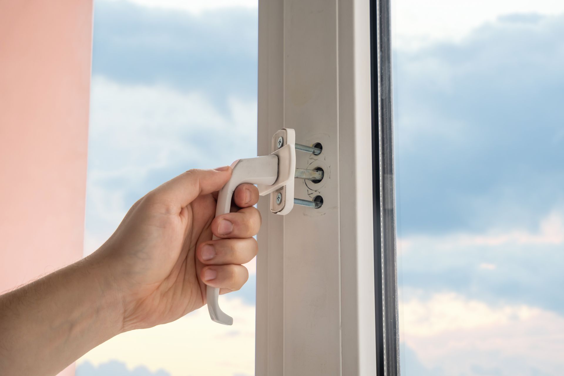 A hand operating a white crank handle to open a window with a cloudy sky visible through the glass A hand operating a white crank handle to open a window with a cloudy sky visible through the glass
