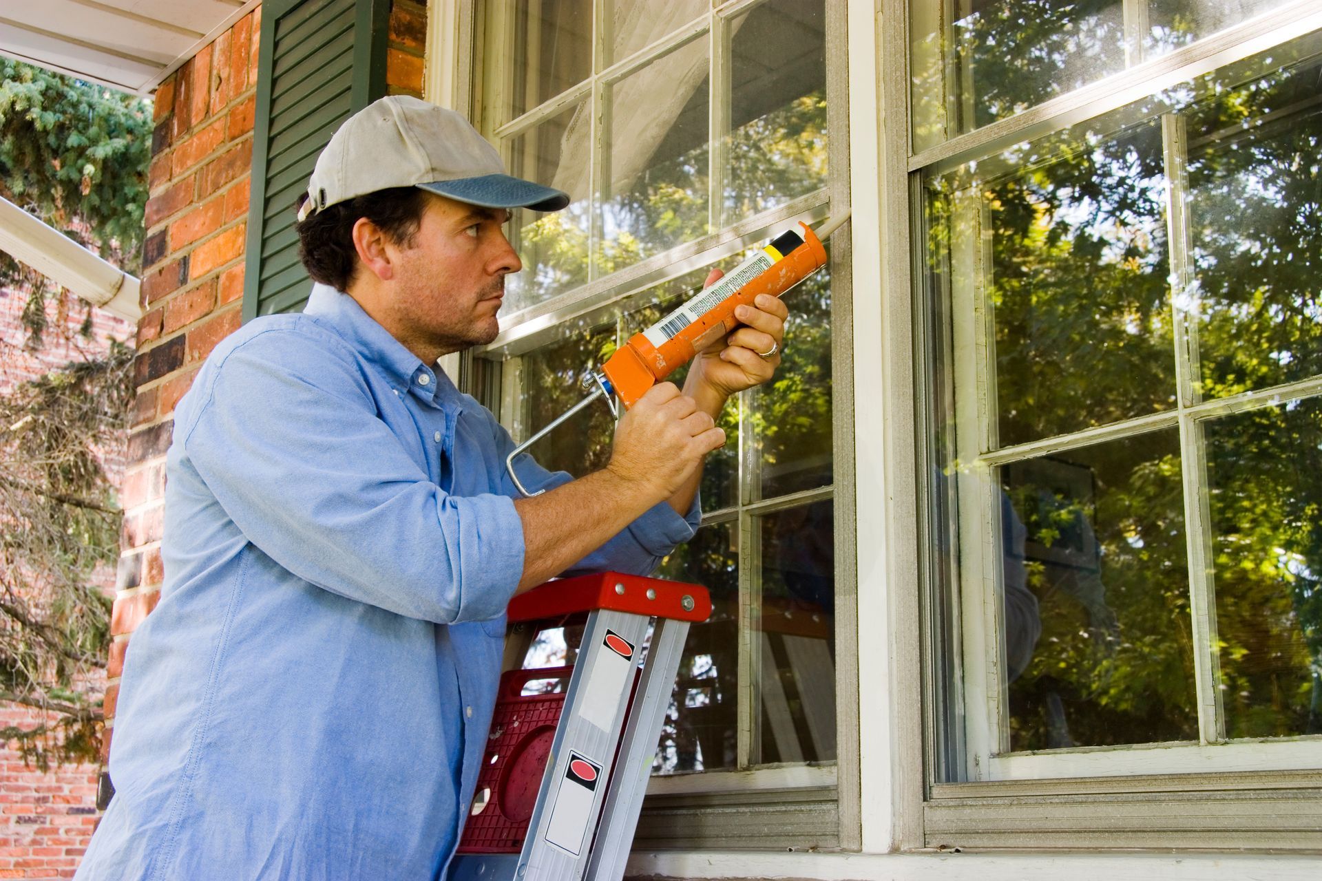 A man on a ladder is chalking an exterior window border.
