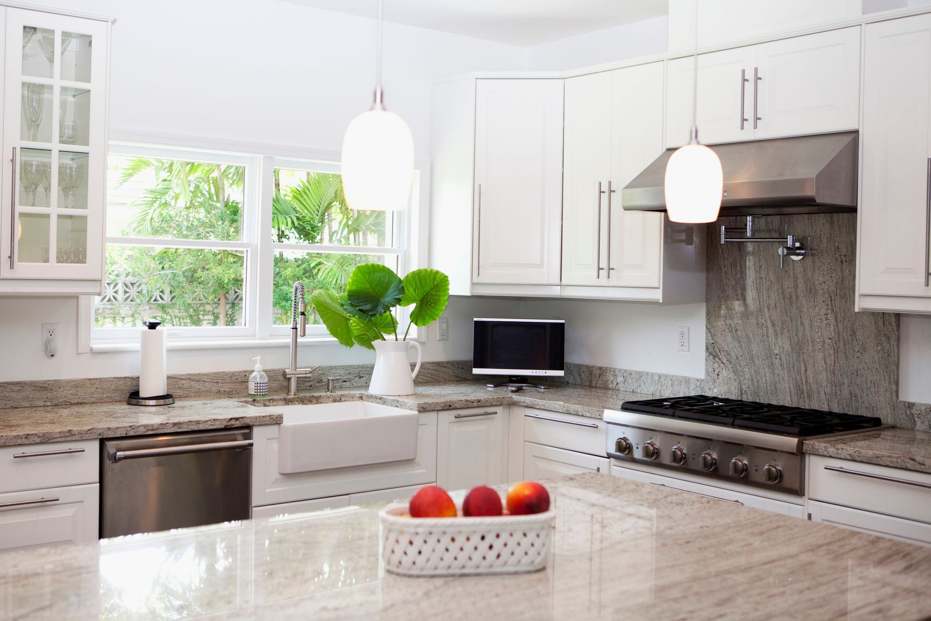 Bright white kitchen with granite countertops, stainless steel appliances, and a window overlooking greenery.