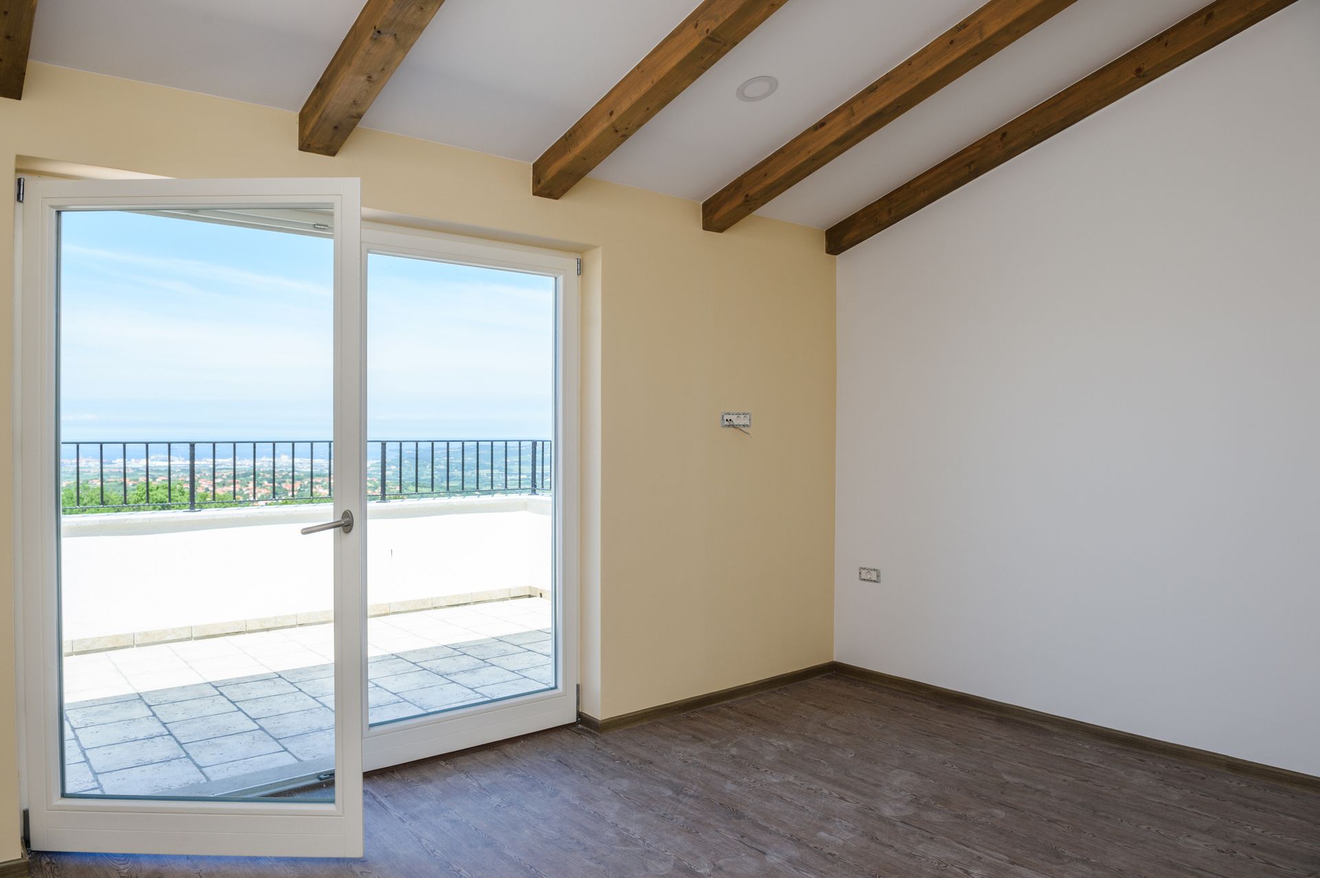 Empty room with open door to a sunny balcony overlooking the ocean.