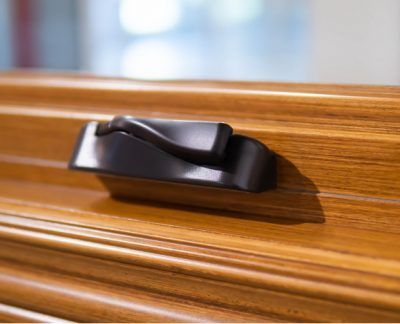 Black window latch on a wooden frame, resting on a windowsill.