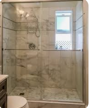 Glass shower with marble tile, a window, and a toilet in a bathroom.