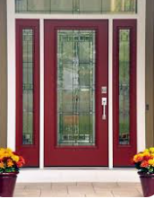 Red front door with sidelights, flowers in pots, and white trim.