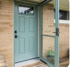 Blue front door with screen door, in front of a brick building.