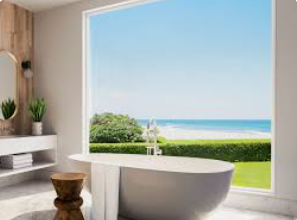 Bathroom with a view of the ocean, featuring a freestanding tub, vanity, and large window with blue sky.
