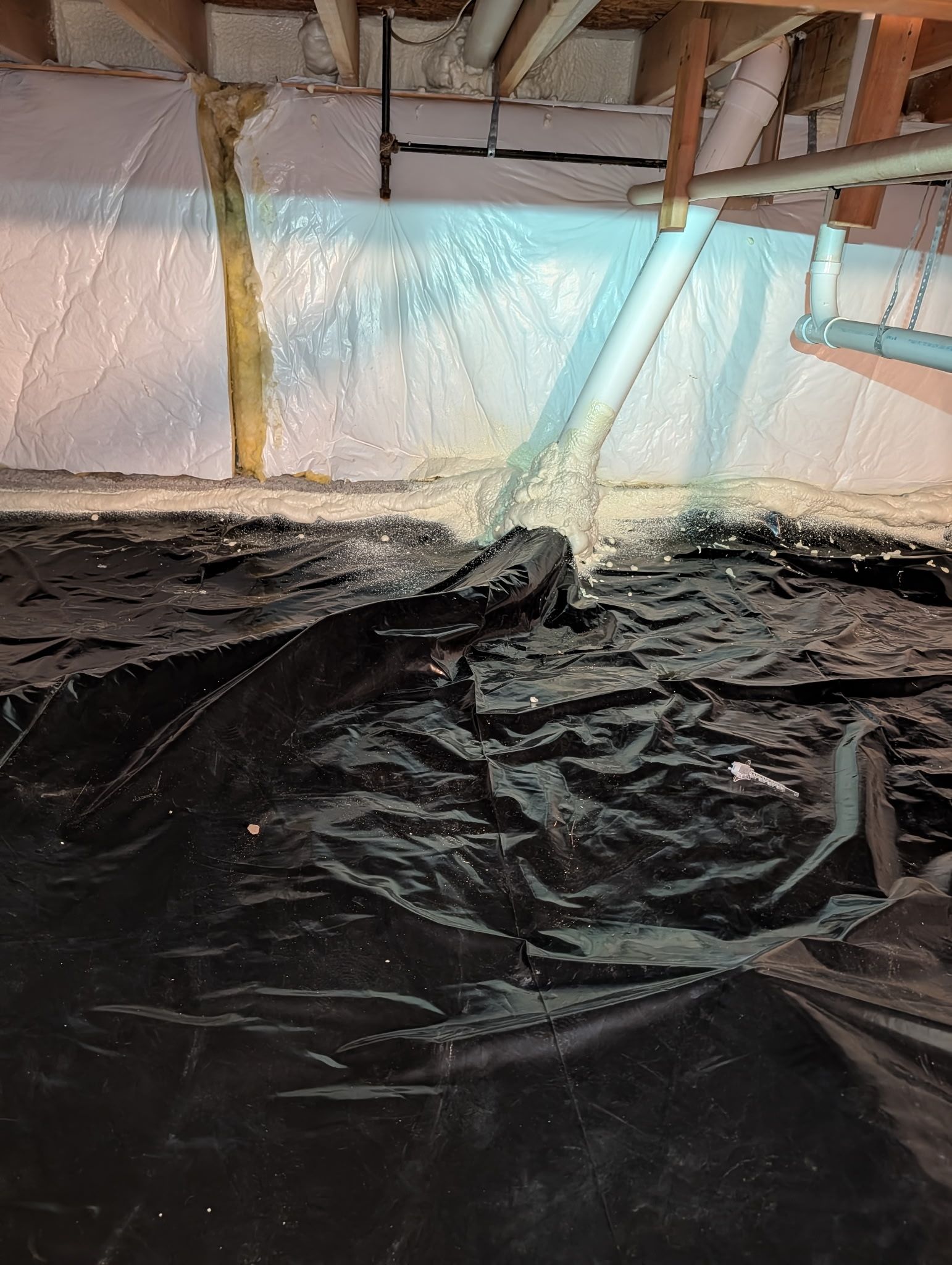 Black plastic sheeting on a floor beneath exposed pipes, with a bright blue tarp or insulation in the background.