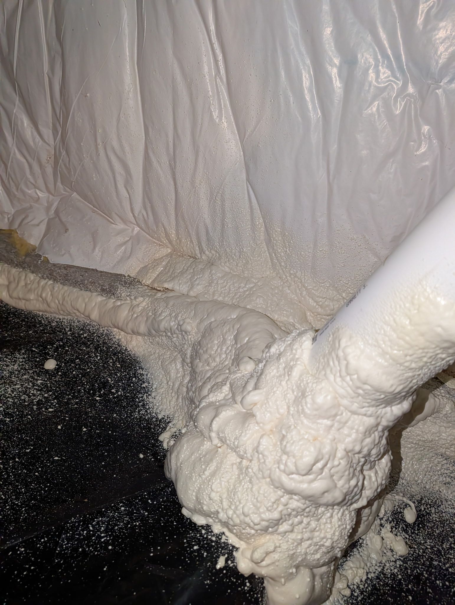 Foam insulation sprayed on wall and pipe in a construction space