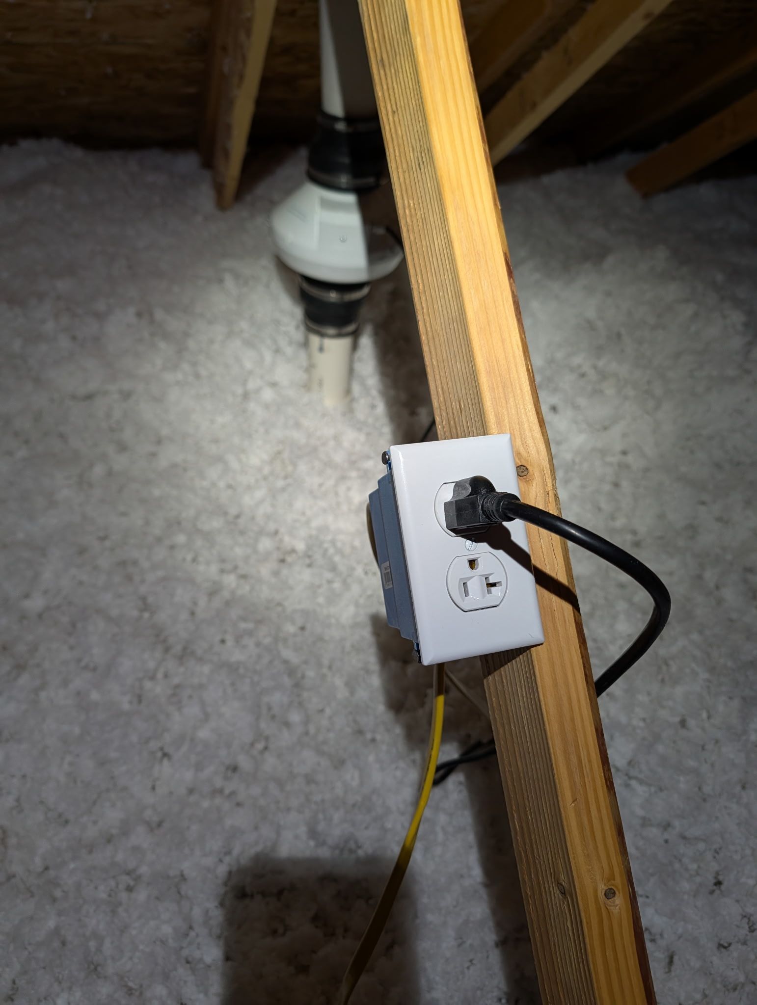 Electrical outlet and cords attached to a wooden beam on a carpeted floor under furniture.