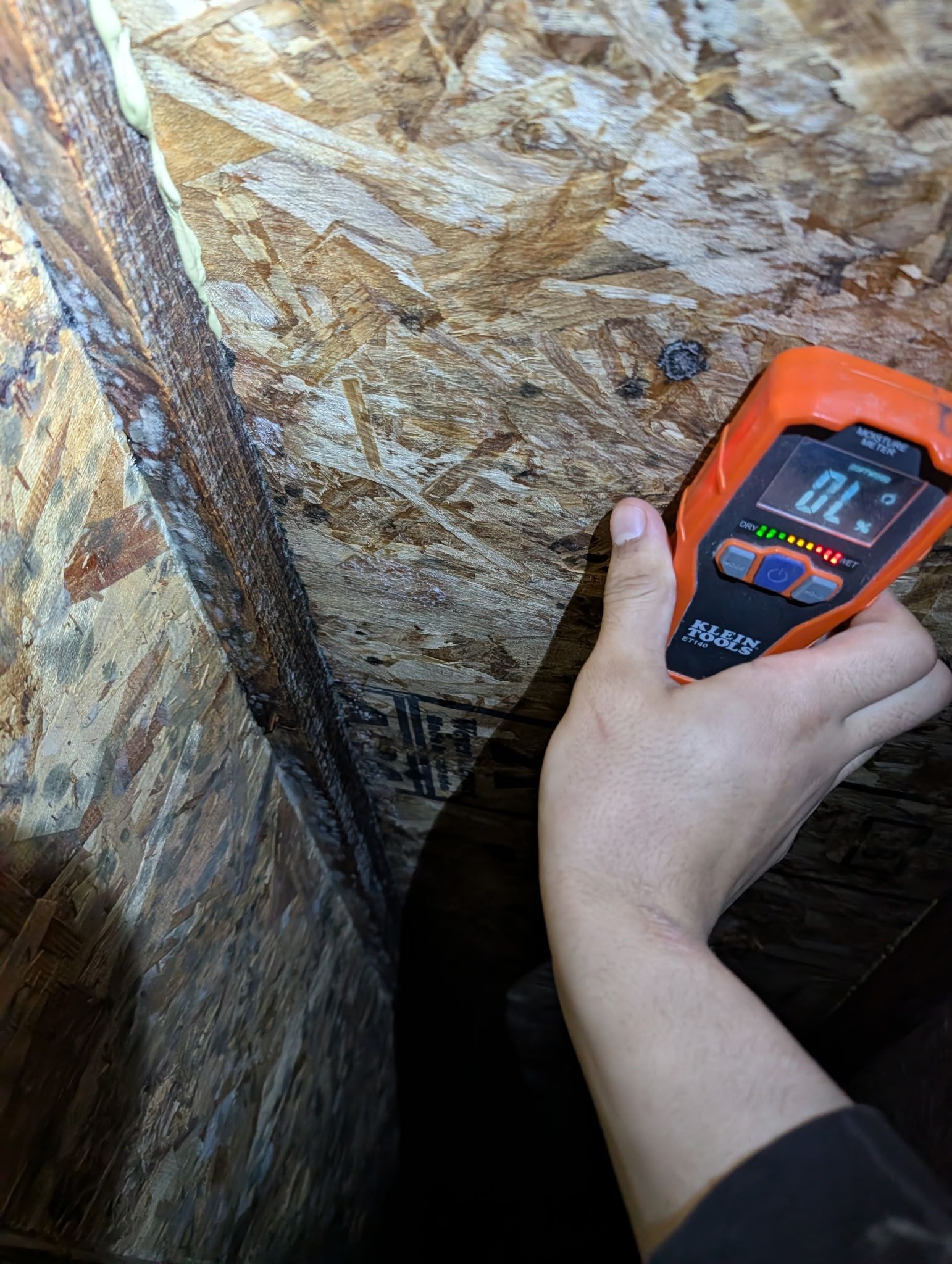 Handheld orange meter being used to measure a rock wall in a narrow cave-like space