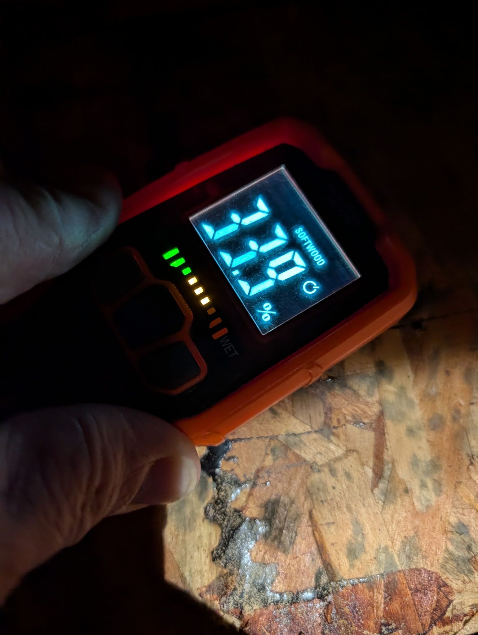 Hand holding an orange pulse oximeter showing oxygen saturation and pulse reading on a fingertip