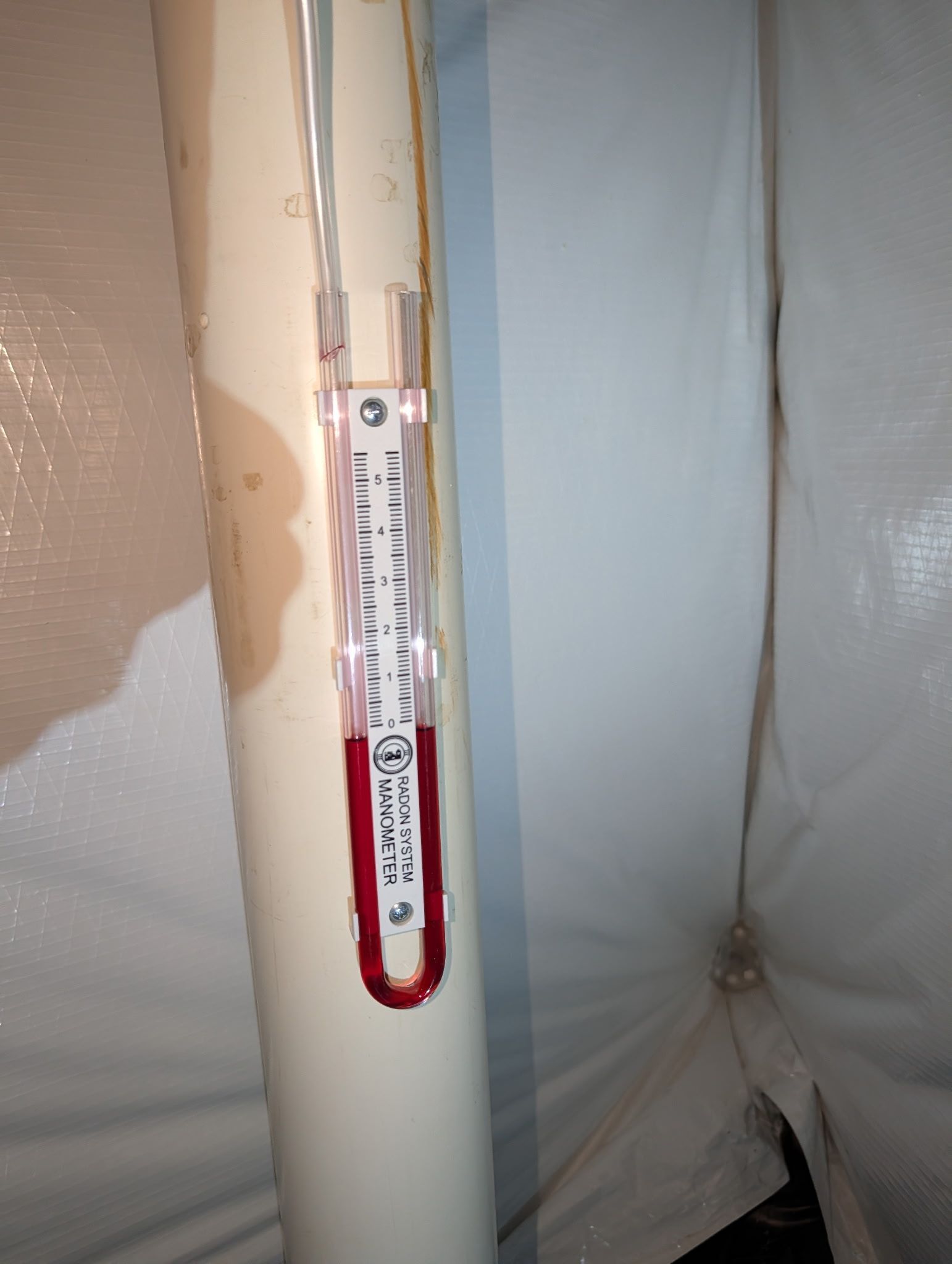 Thermometer clipped to a white pipe against a plastic-covered wall.