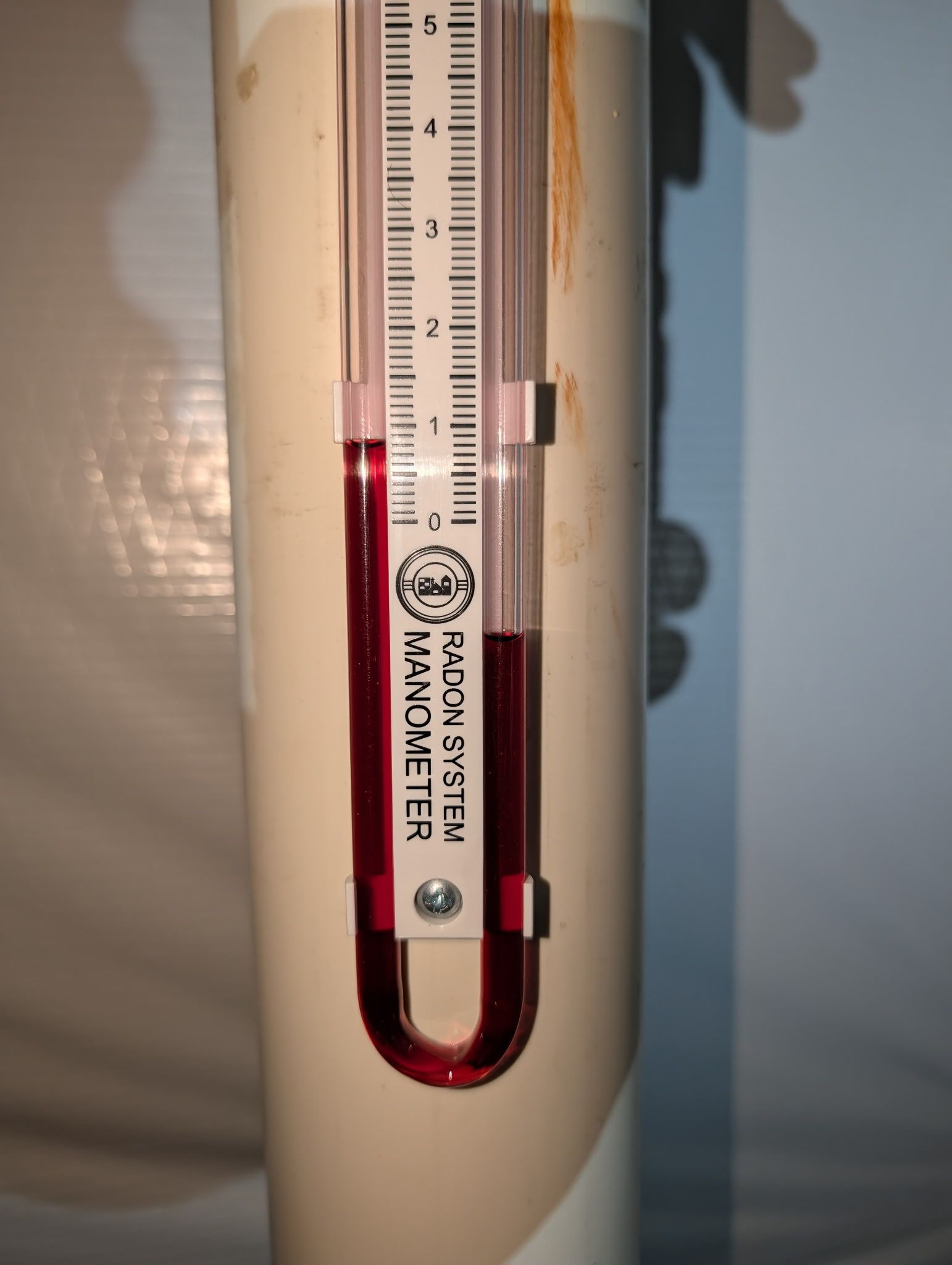 Close-up of a glass thermometer with red liquid against a light wall.