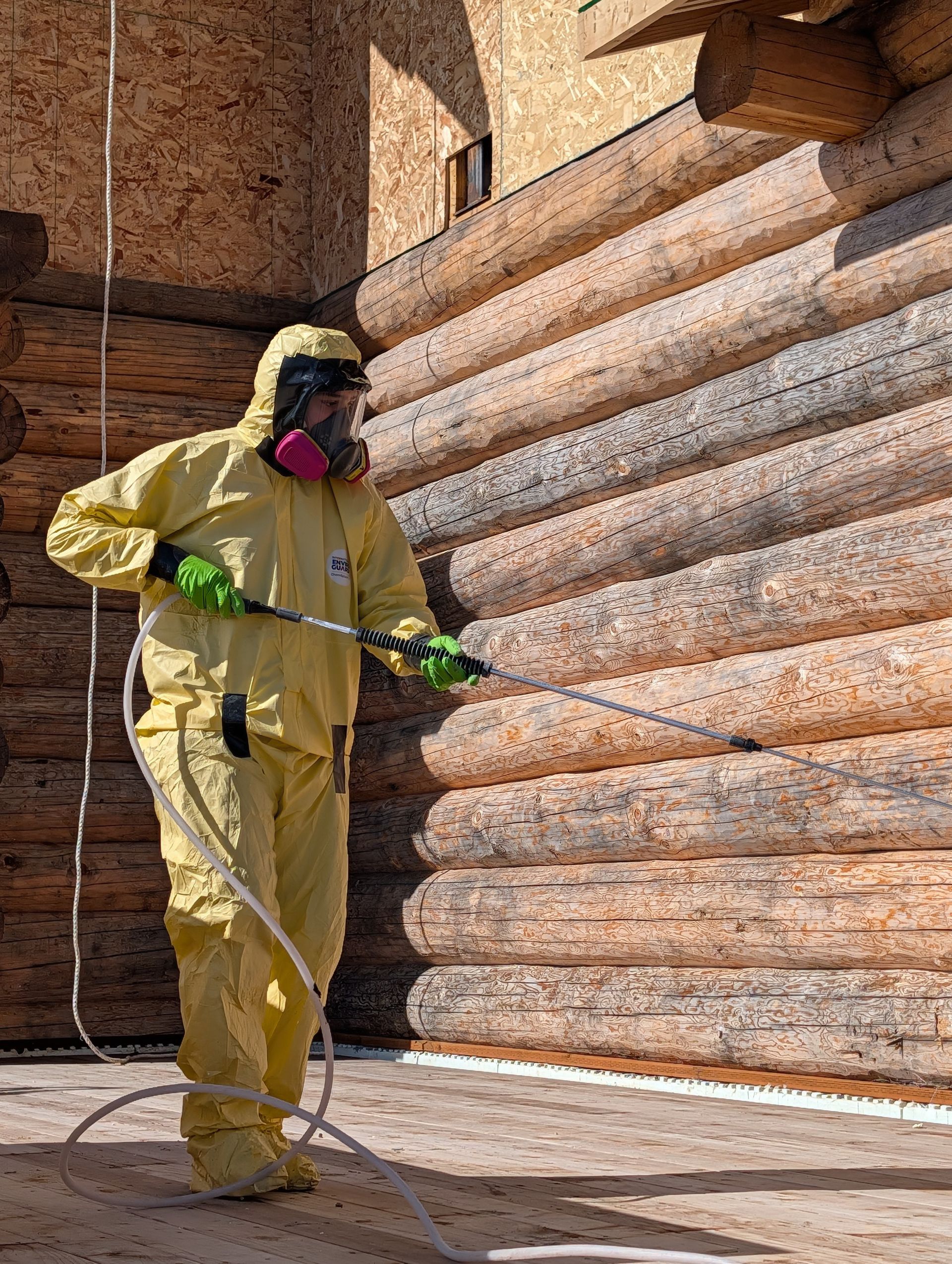 Person in yellow protective suit pressure-washing a stone wall and floor.