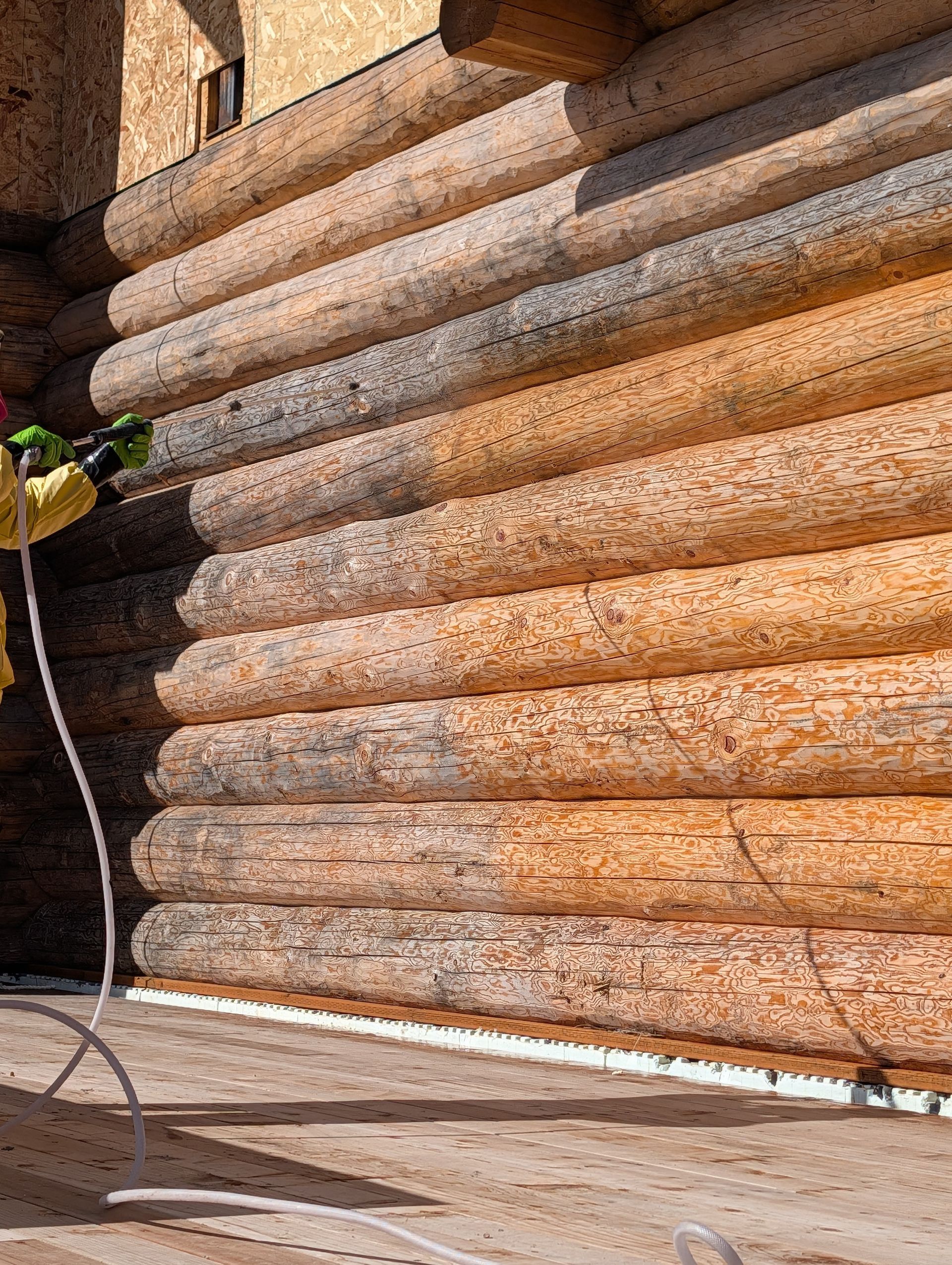 Close-up of stacked rustic log or timber walls with sunlight and a small cable on the left.
