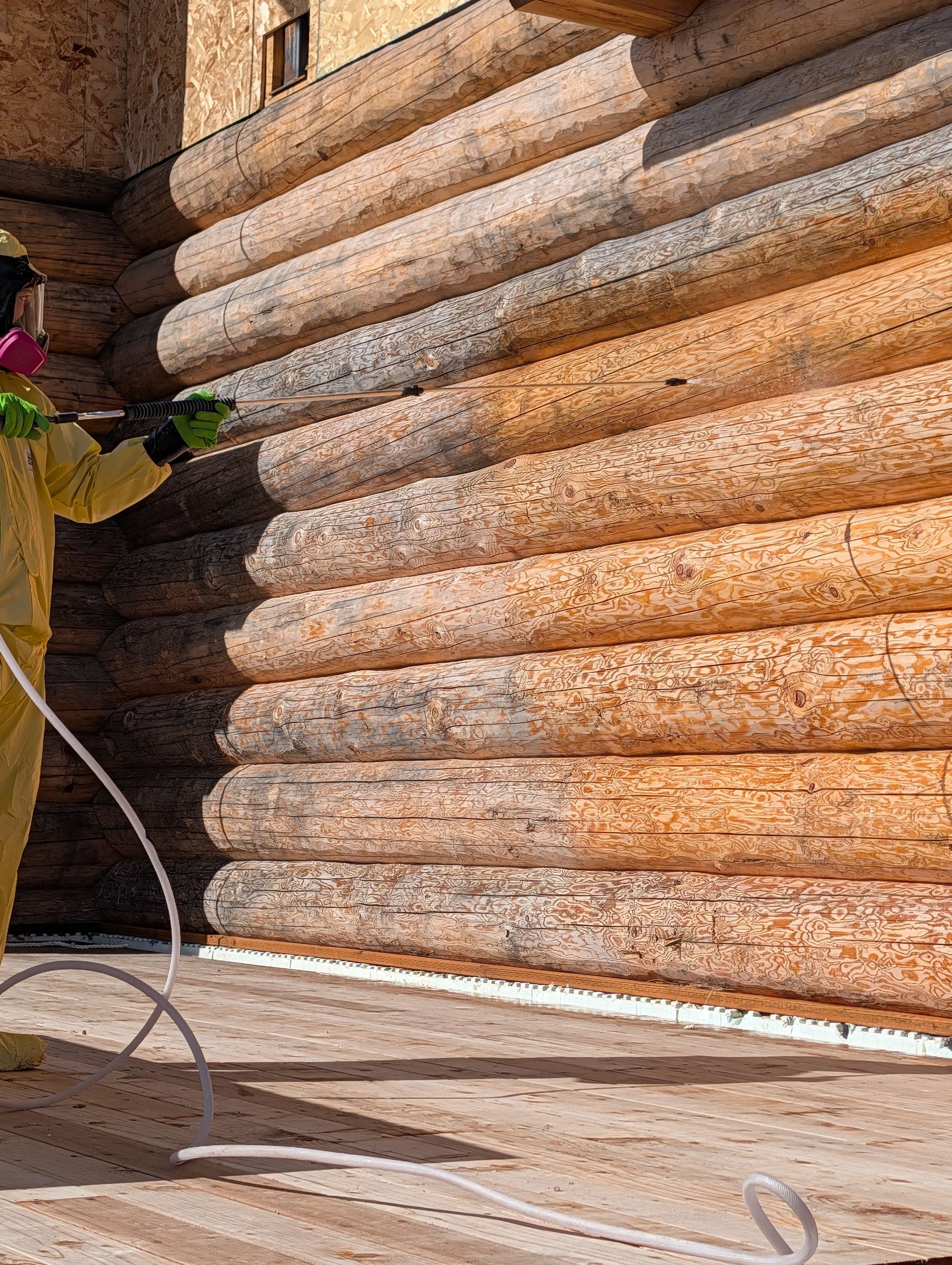 Worker in yellow protective gear spraying a log wall with a hose