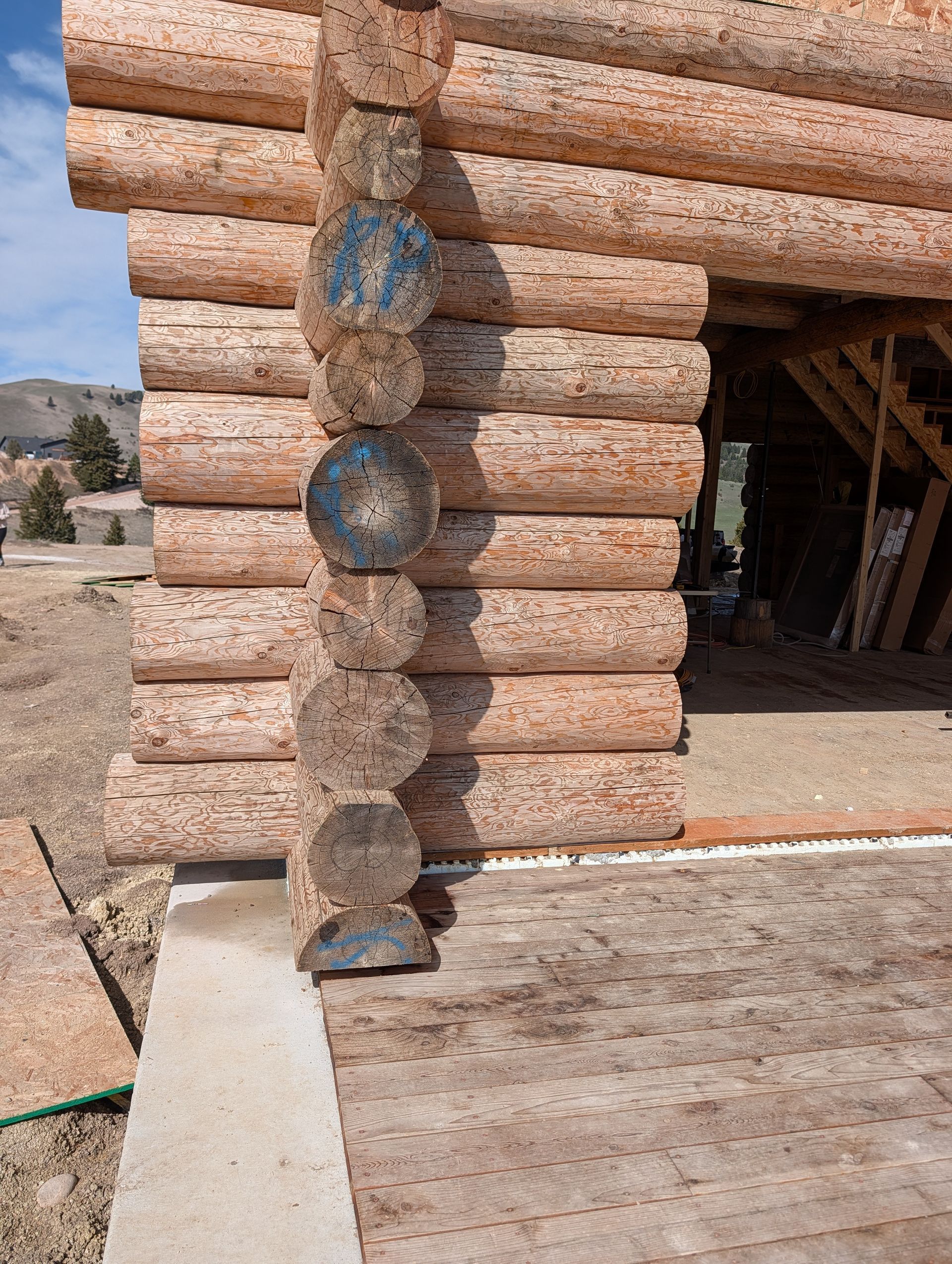 Log cabin wall with decorative blue glass bottles embedded in the corner beside an open doorway