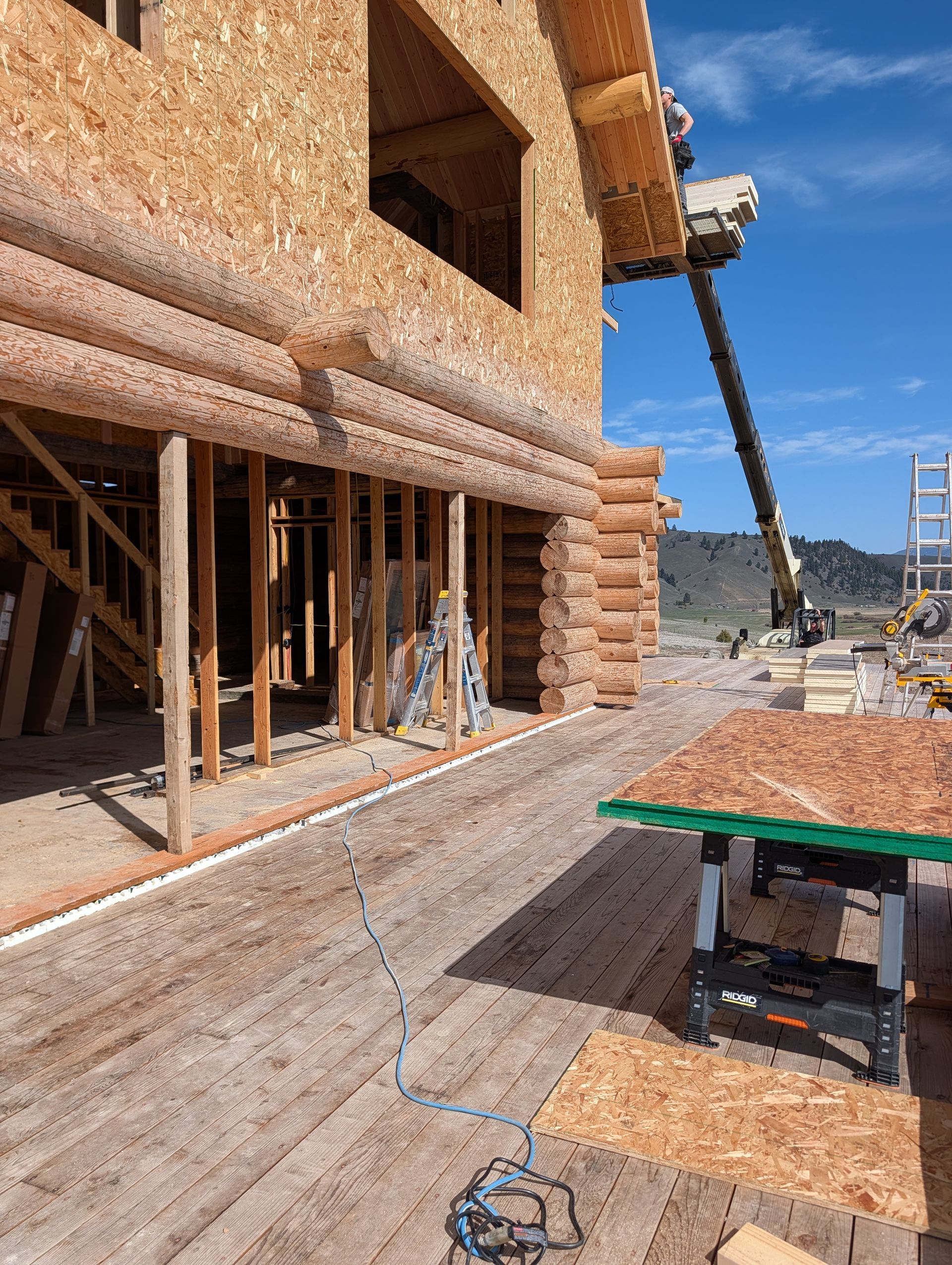 Partially framed house under construction with OSB siding, scaffolding, and a clear blue sky