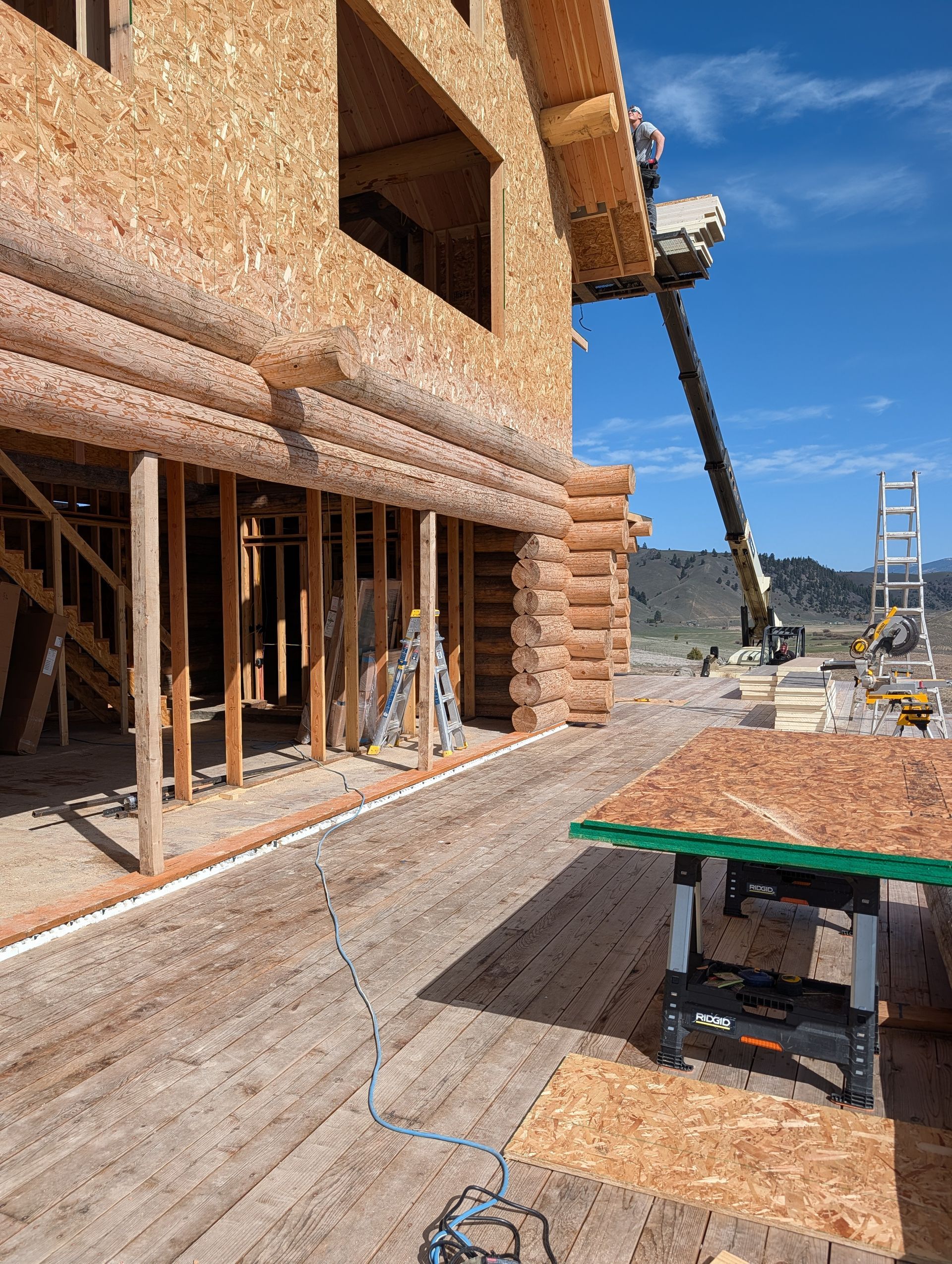Partially built log house exterior with wooden scaffolding and construction materials on a sunny site