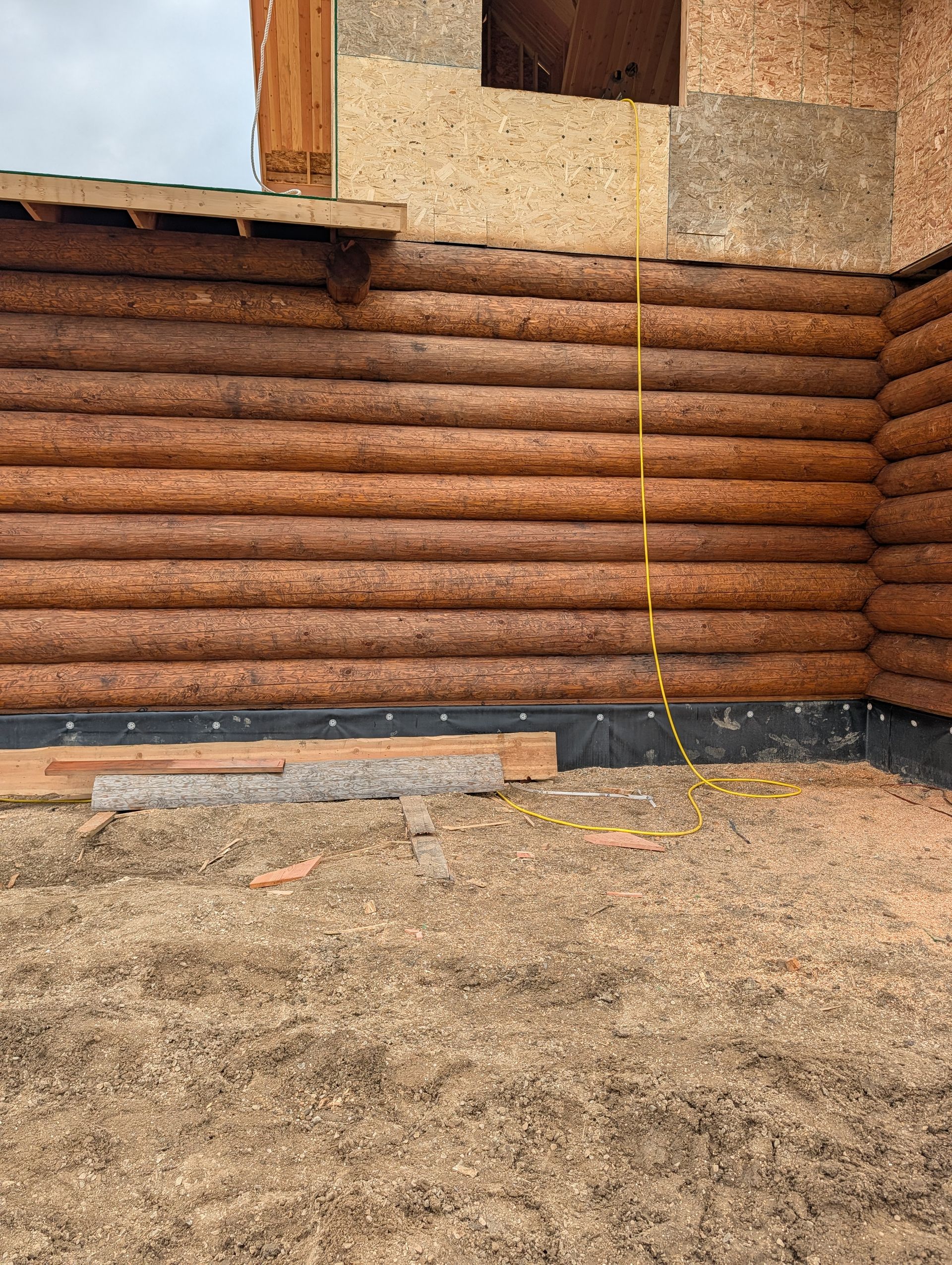 Log cabin exterior with stacked logs, a window, and a gravel ground beneath the wall