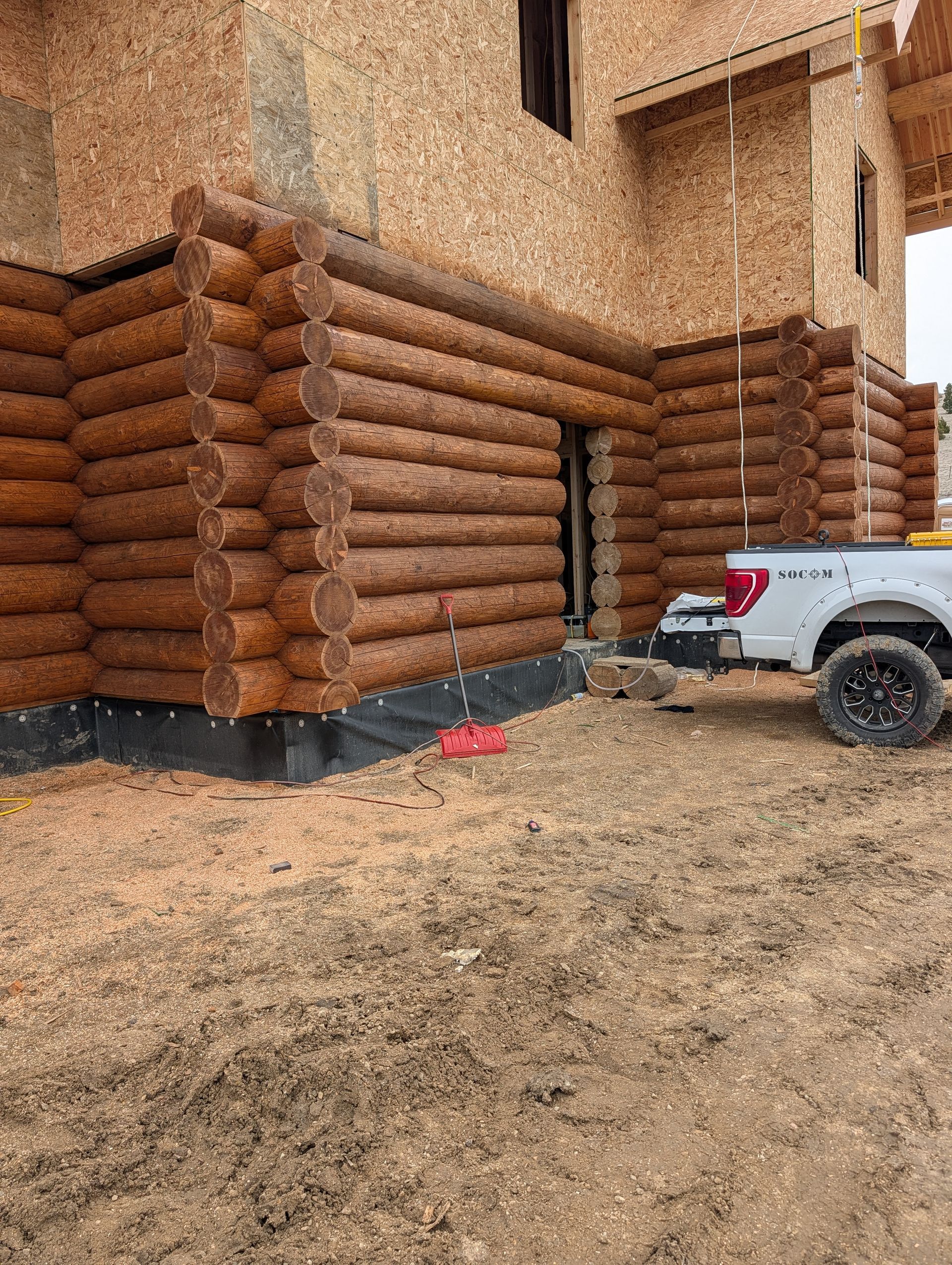 Log cabin wall with timber logs, dripping water, and a white utility vehicle parked beside it