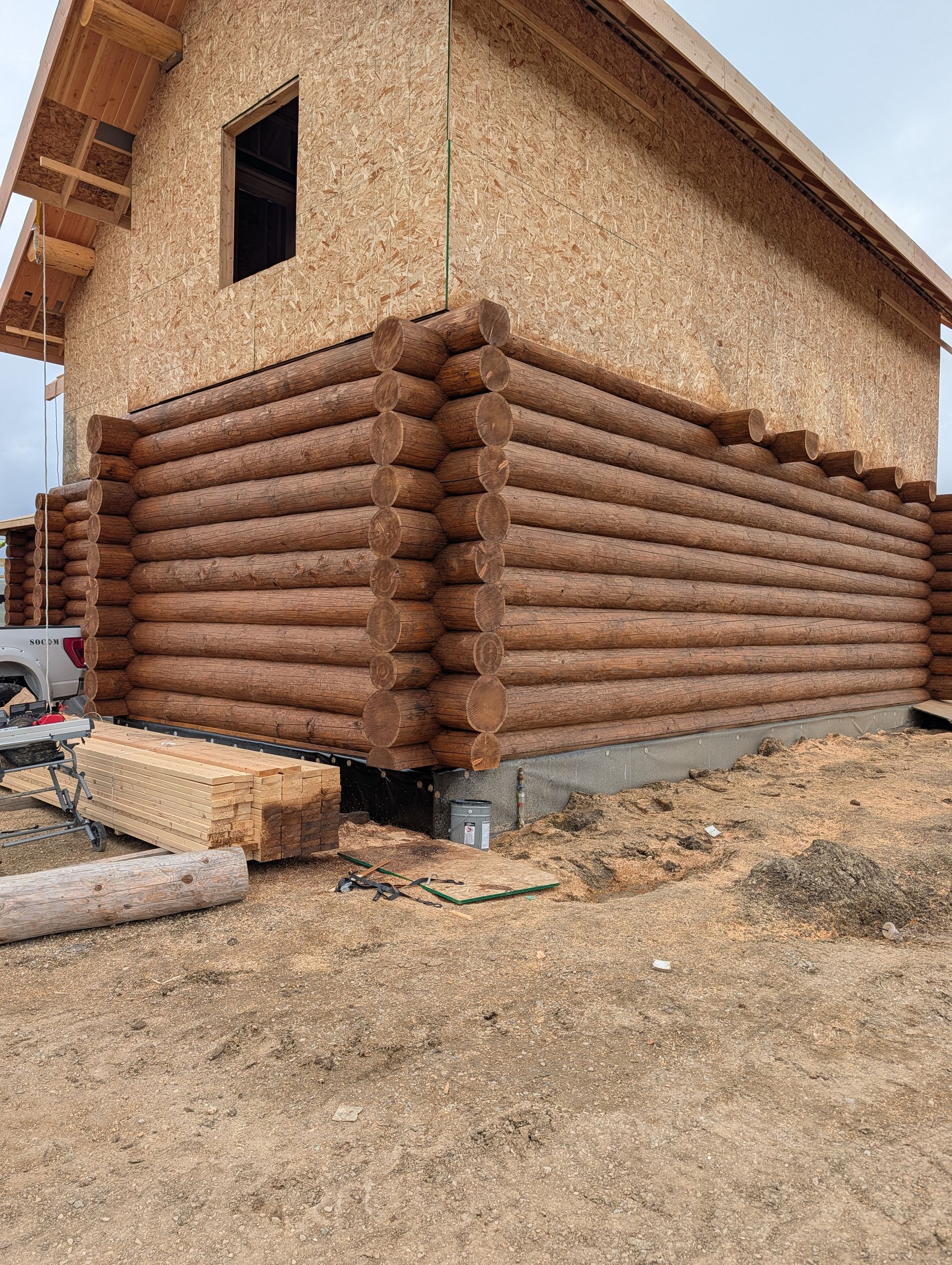 Partially built log house with tan walls and brown timber lower walls on a dirt construction site