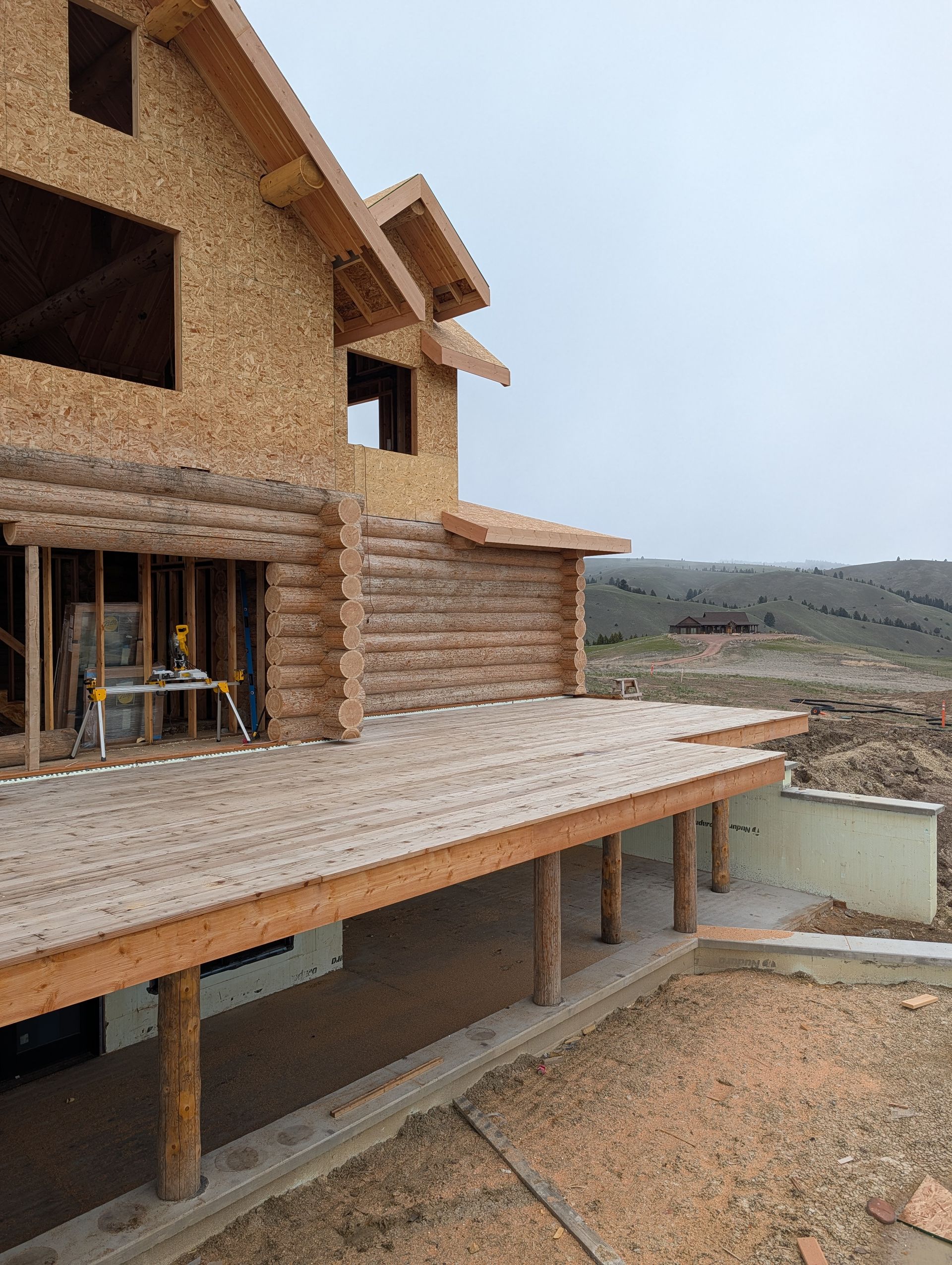 Partially built house with wood framing, stucco walls, and a wraparound porch overlooking a rocky landscape