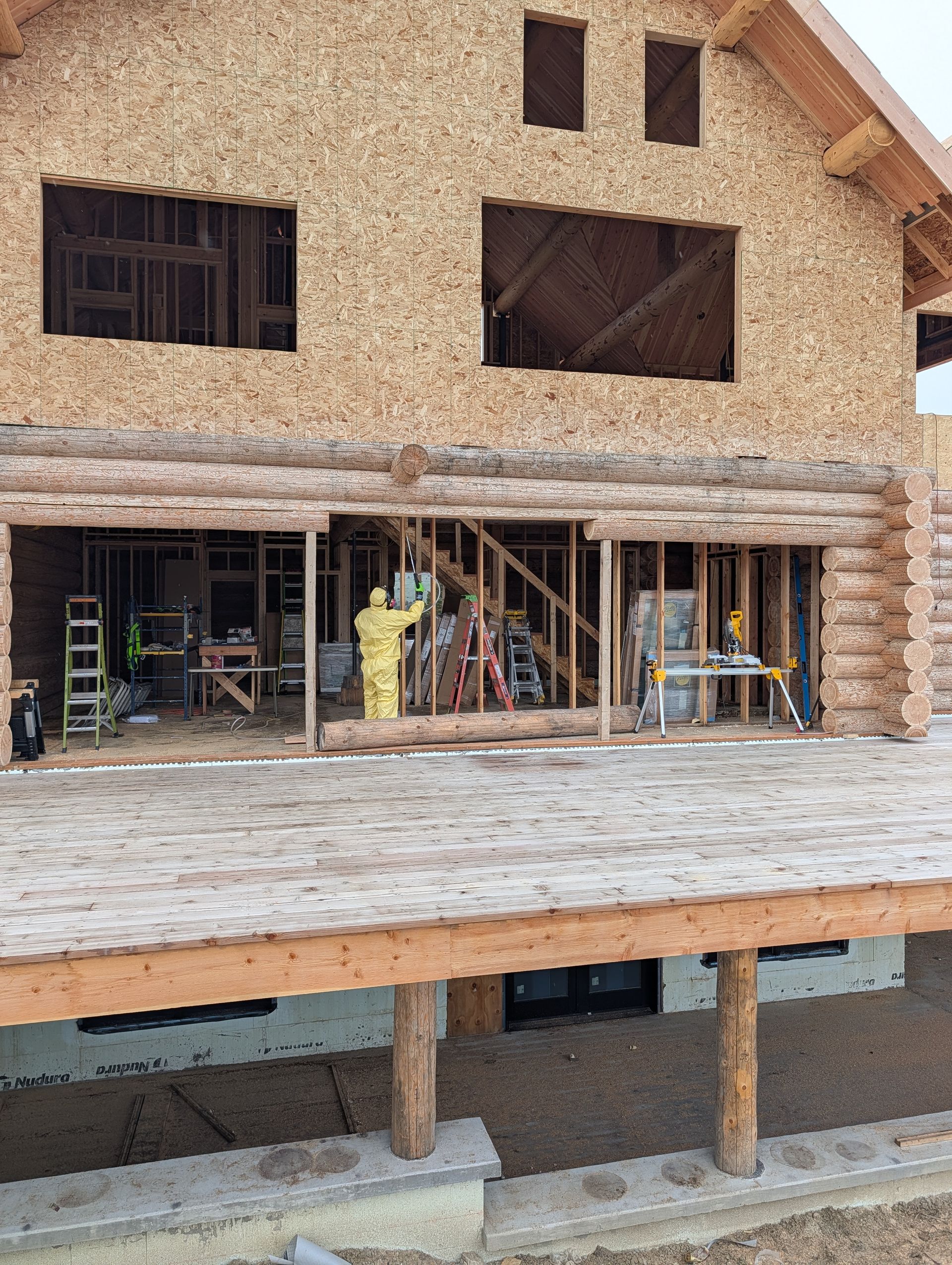 Partially built two-story house with exposed framing, open windows, and workers on the ground floor