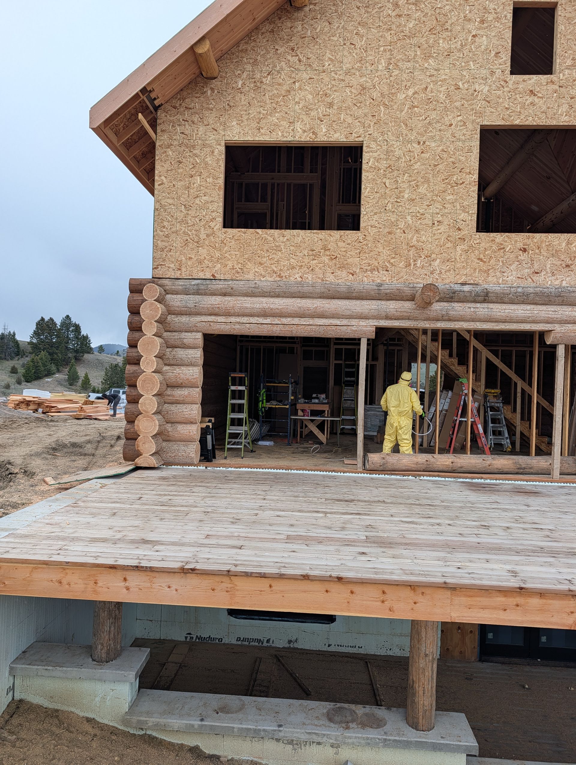 Two-story house under construction with workers in a covered ground-floor area