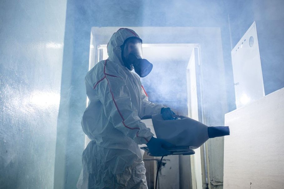 Person in protective suit using a fogging machine inside a misty room