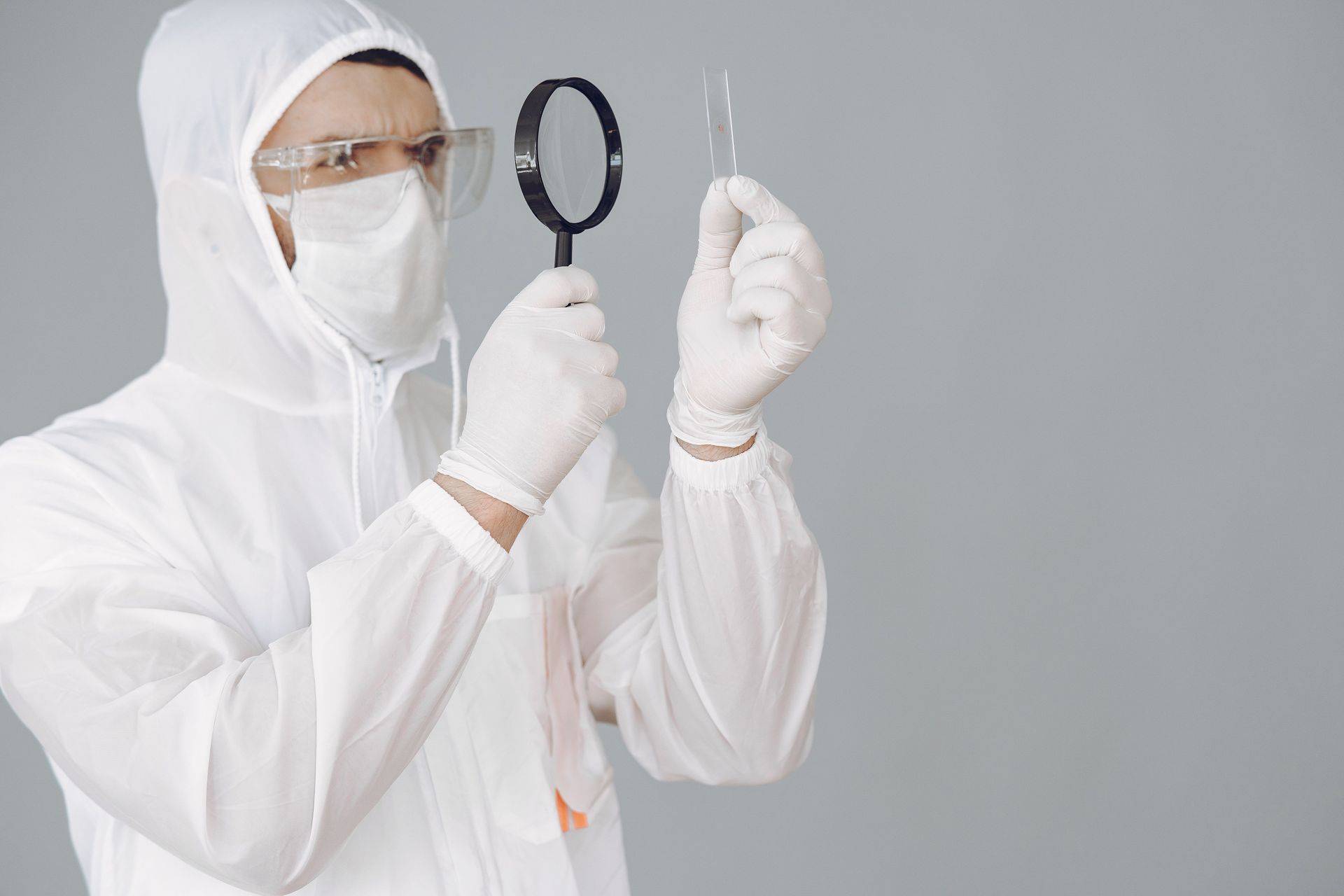 Lab technician in white protective suit examining a sample of mold under a magnifying glass