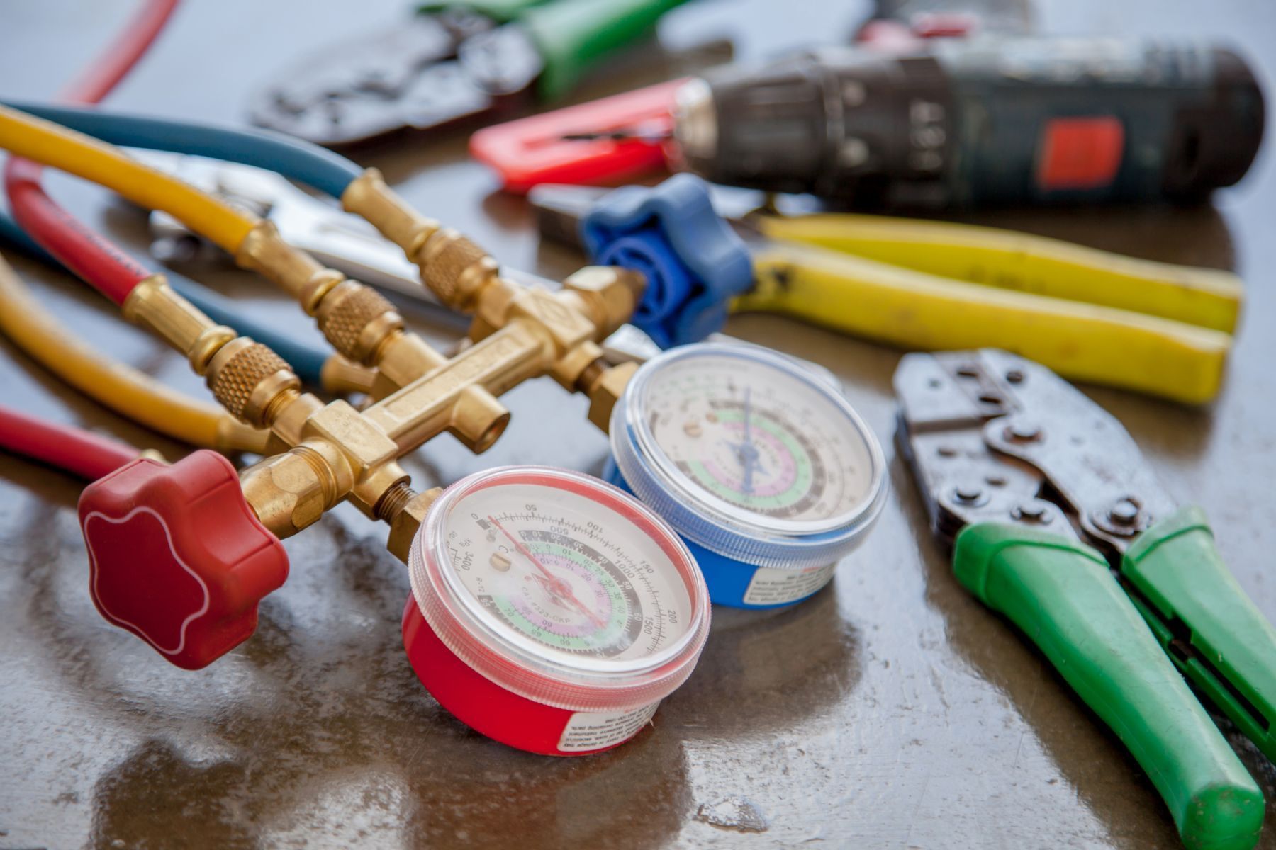 HVAC repair tools: gauges, pliers, screwdrivers, and hoses on a wet surface