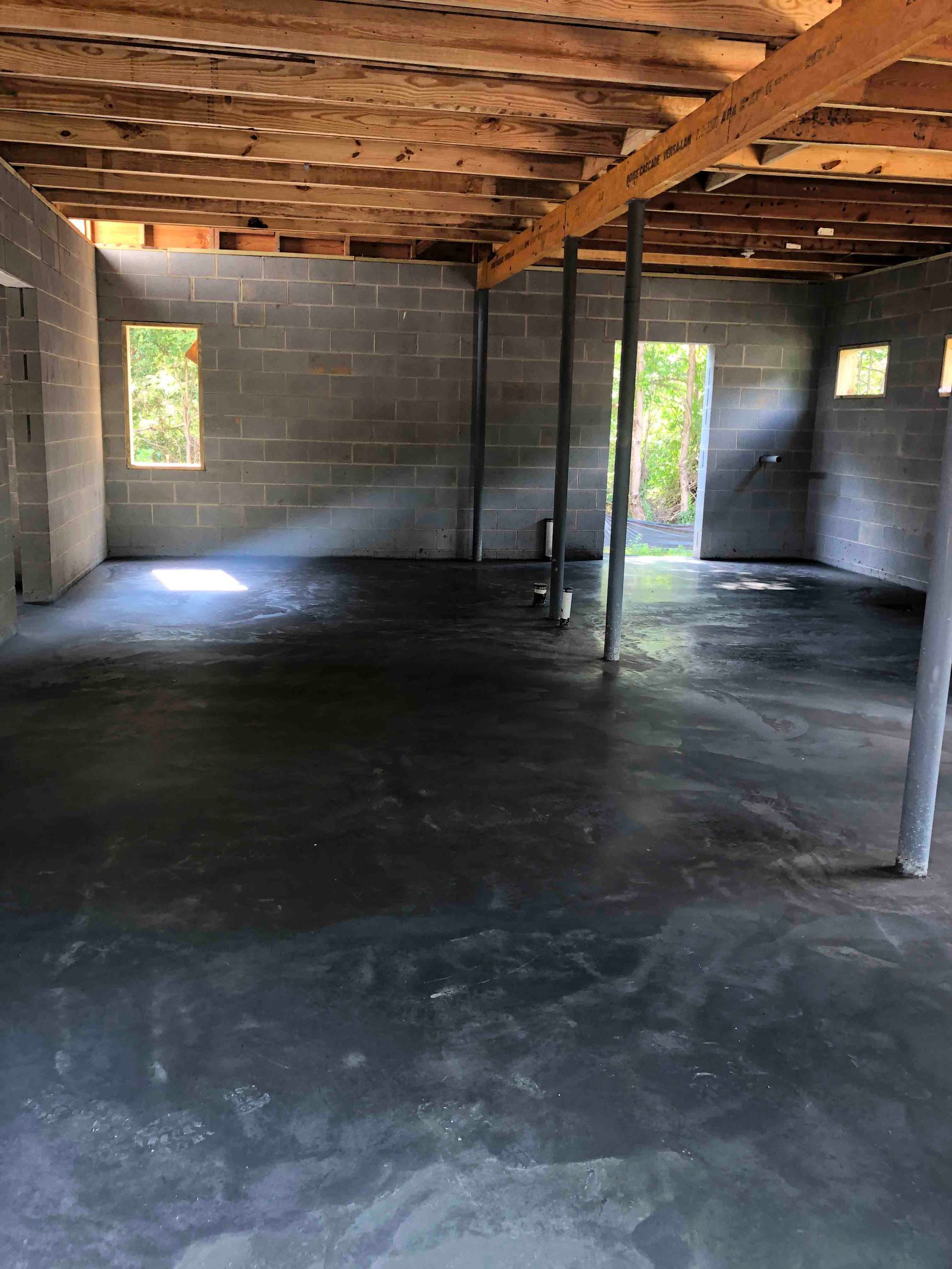 An empty basement with a concrete floor and wooden beams.
