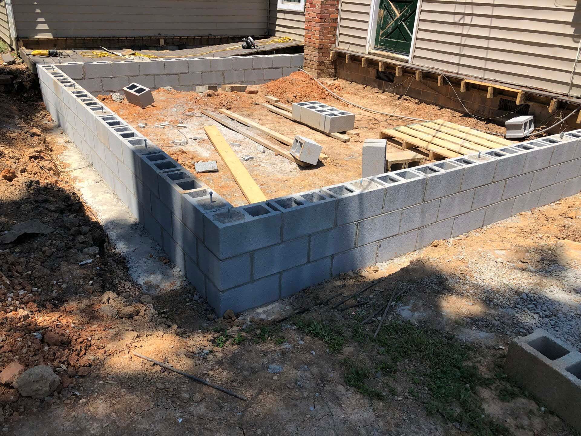 A brick wall is being built in the dirt in front of a house.