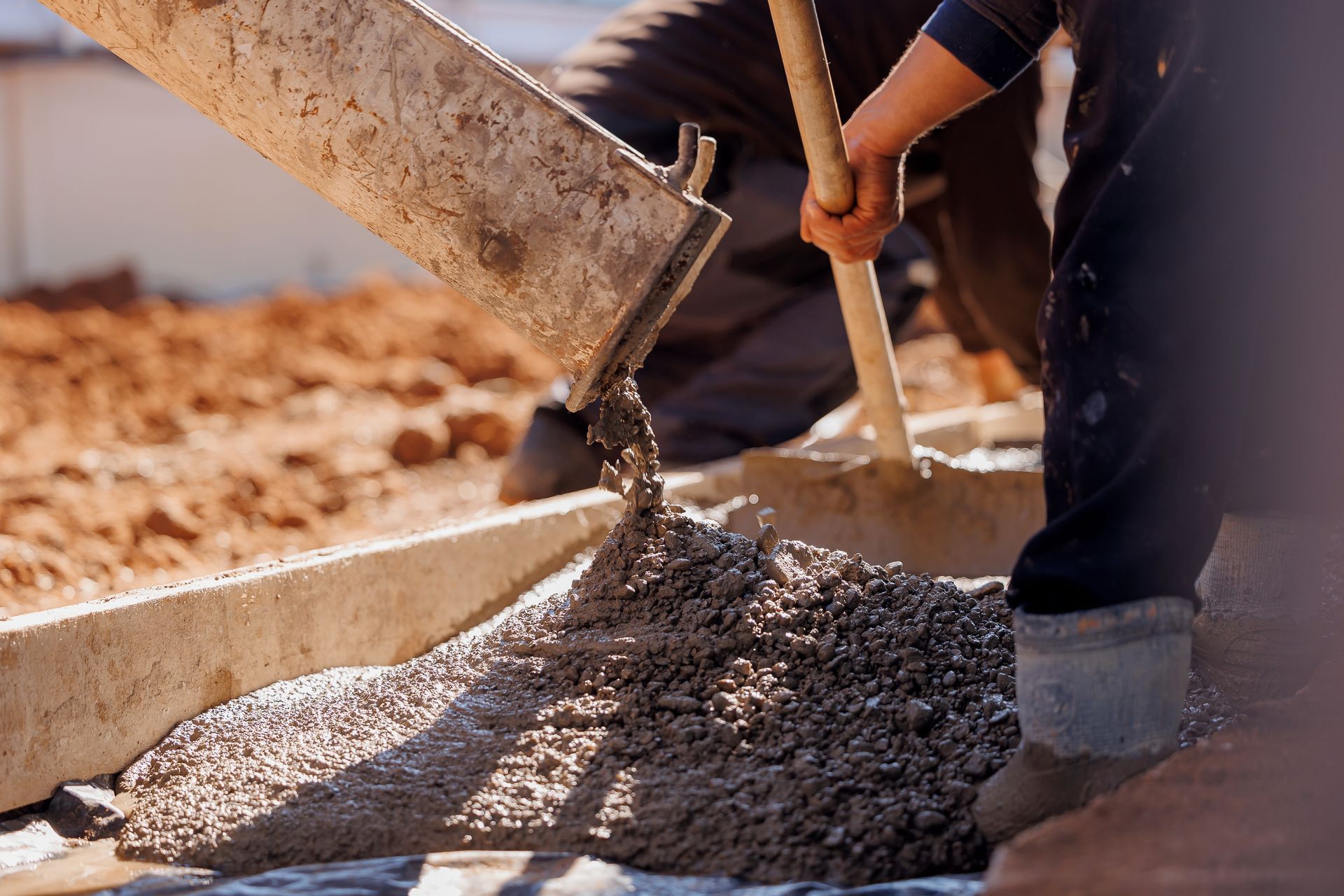 A man is pouring concrete into a hole with a shovel.