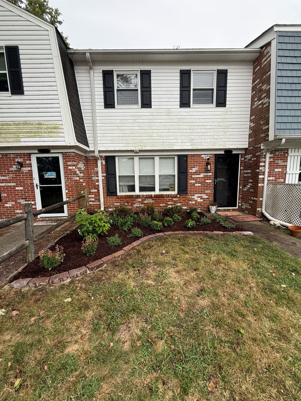 Front of a brick-and-white townhouse with a small grass lawn and shrub bed underneath the windows.