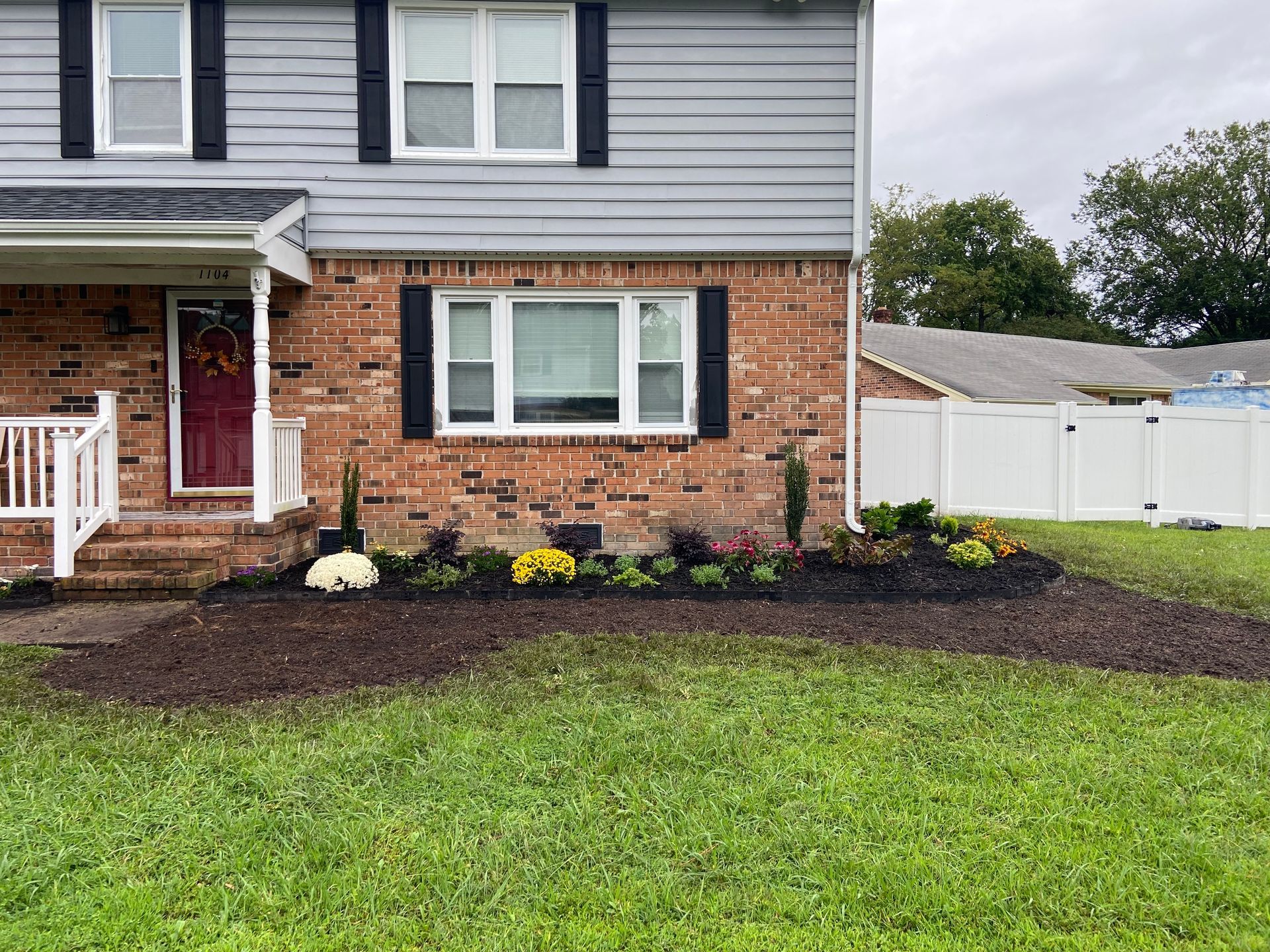 Suburban house exterior with brick and gray siding, front porch, flower bed, and green lawn