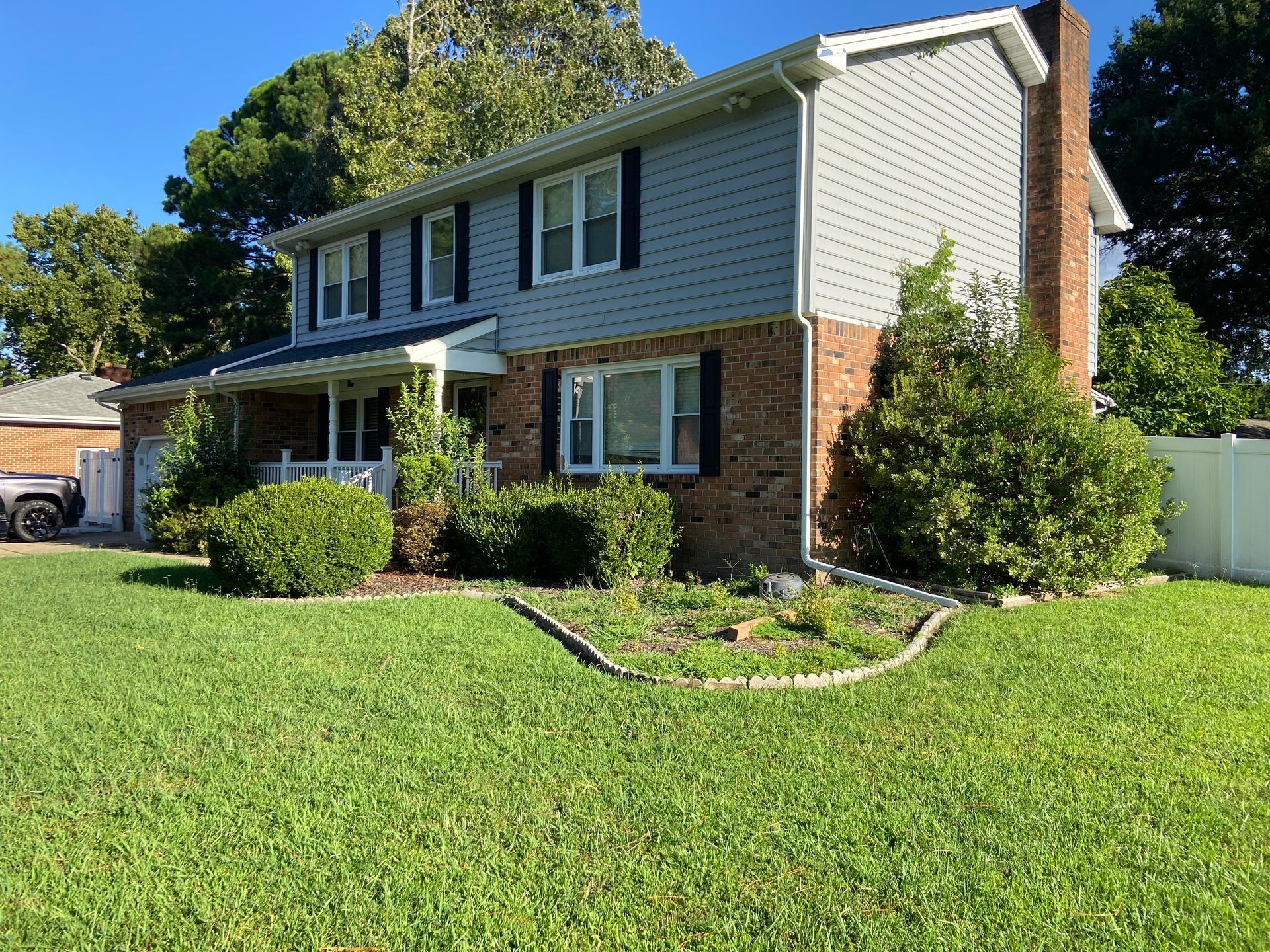Two-story brick and siding suburban house with a green lawn and trees in front