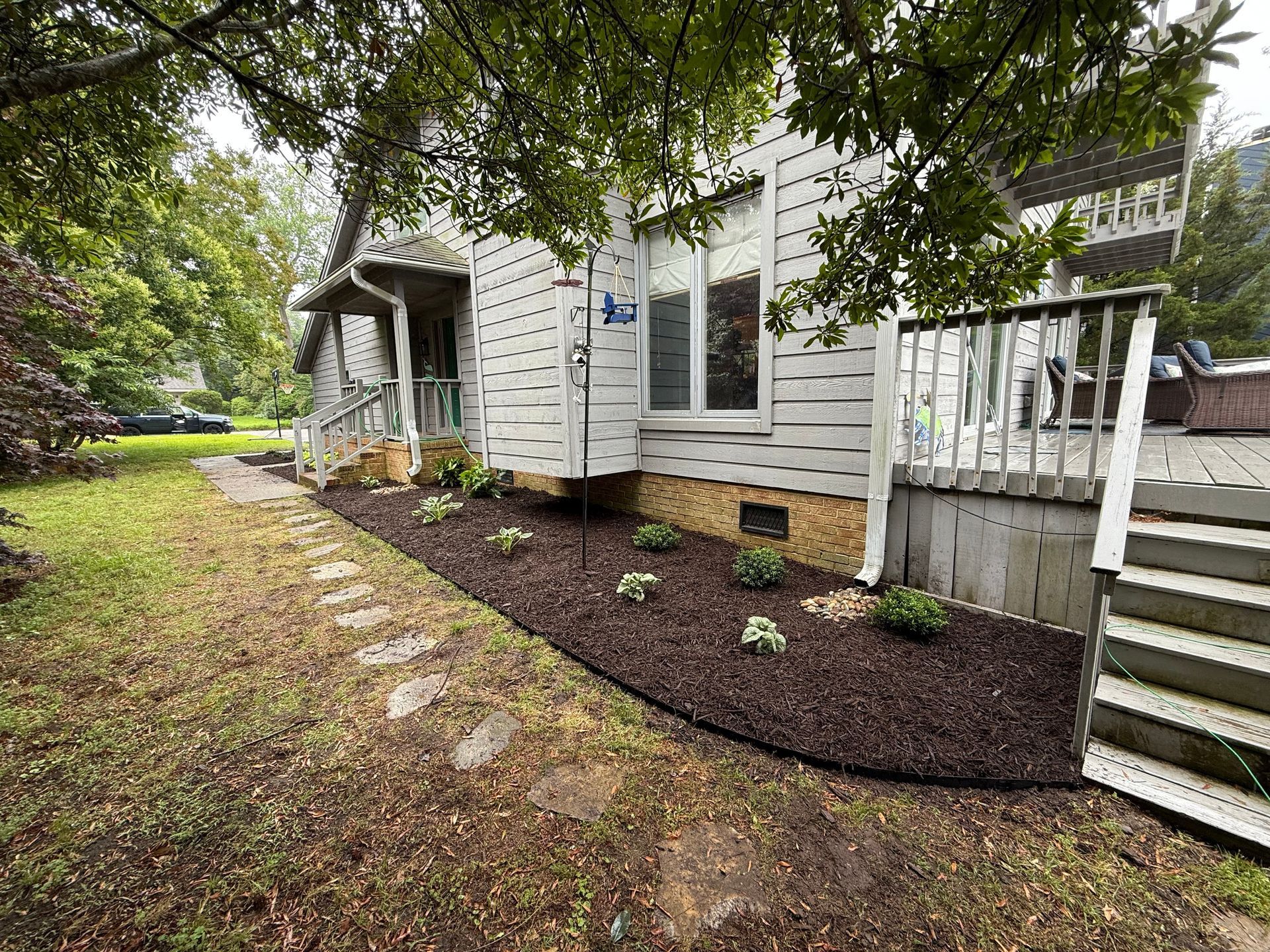 Front yard landscaping with new mulch, small shrubs, stone border, and a house exterior.