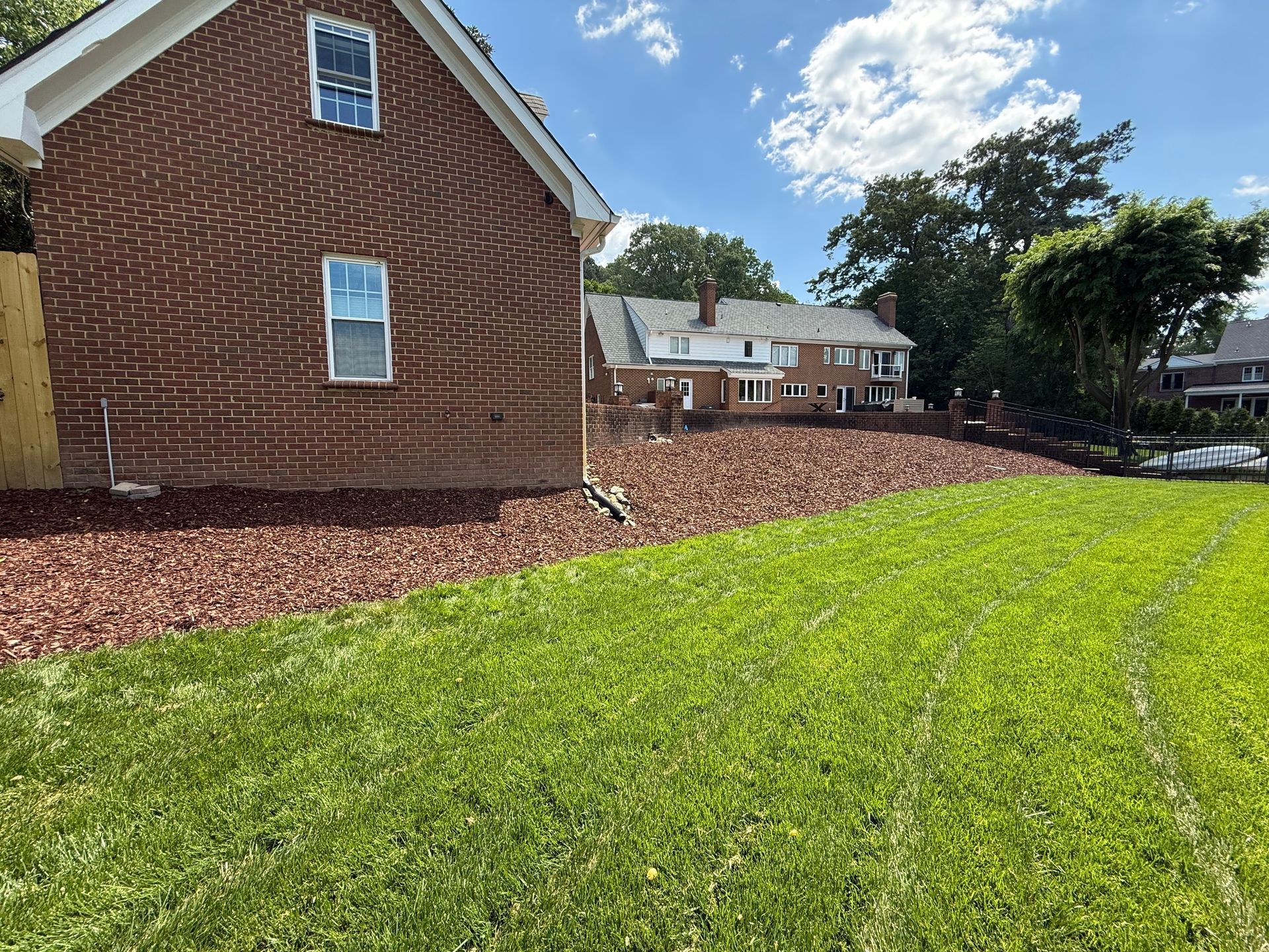 Brick house beside green lawn and mulch beds under a sunny blue sky
